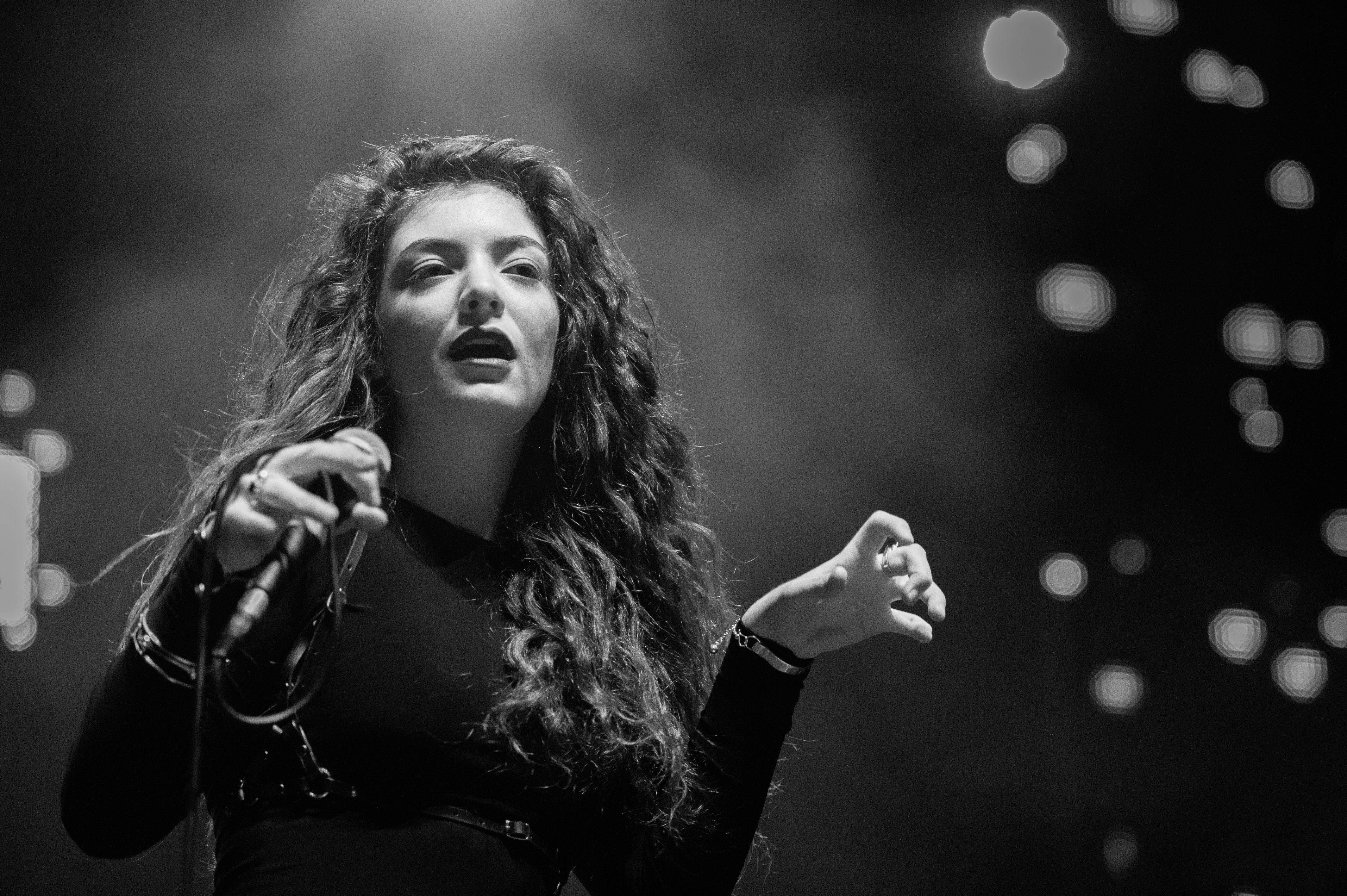 Lorde 桌布 壁紙 — 一張黑白照片，一位長捲髮女歌手在戲劇性燈光下熱情地在舞台上表演。