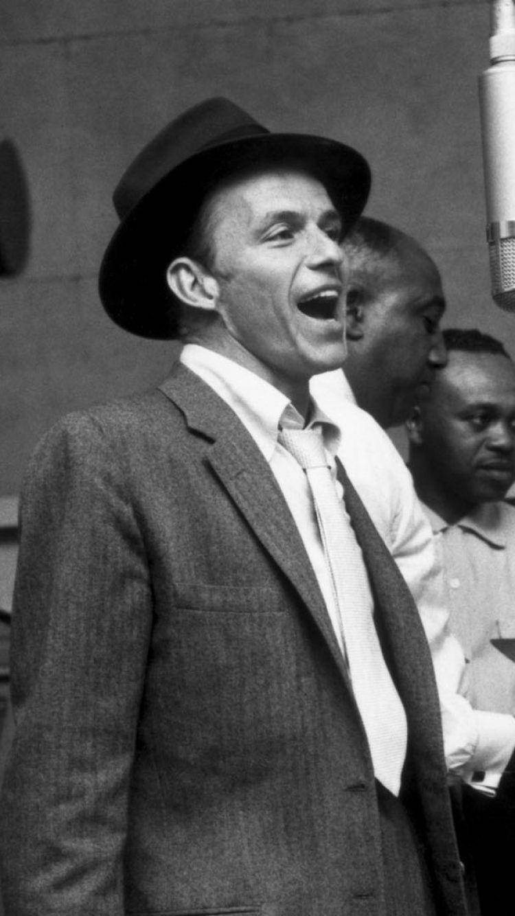 Sinatra 桌布 壁紙 — 一張黑白照片，一名戴著紳士帽、身穿西裝的男子，正充滿激情地對著復古麥克風唱歌。