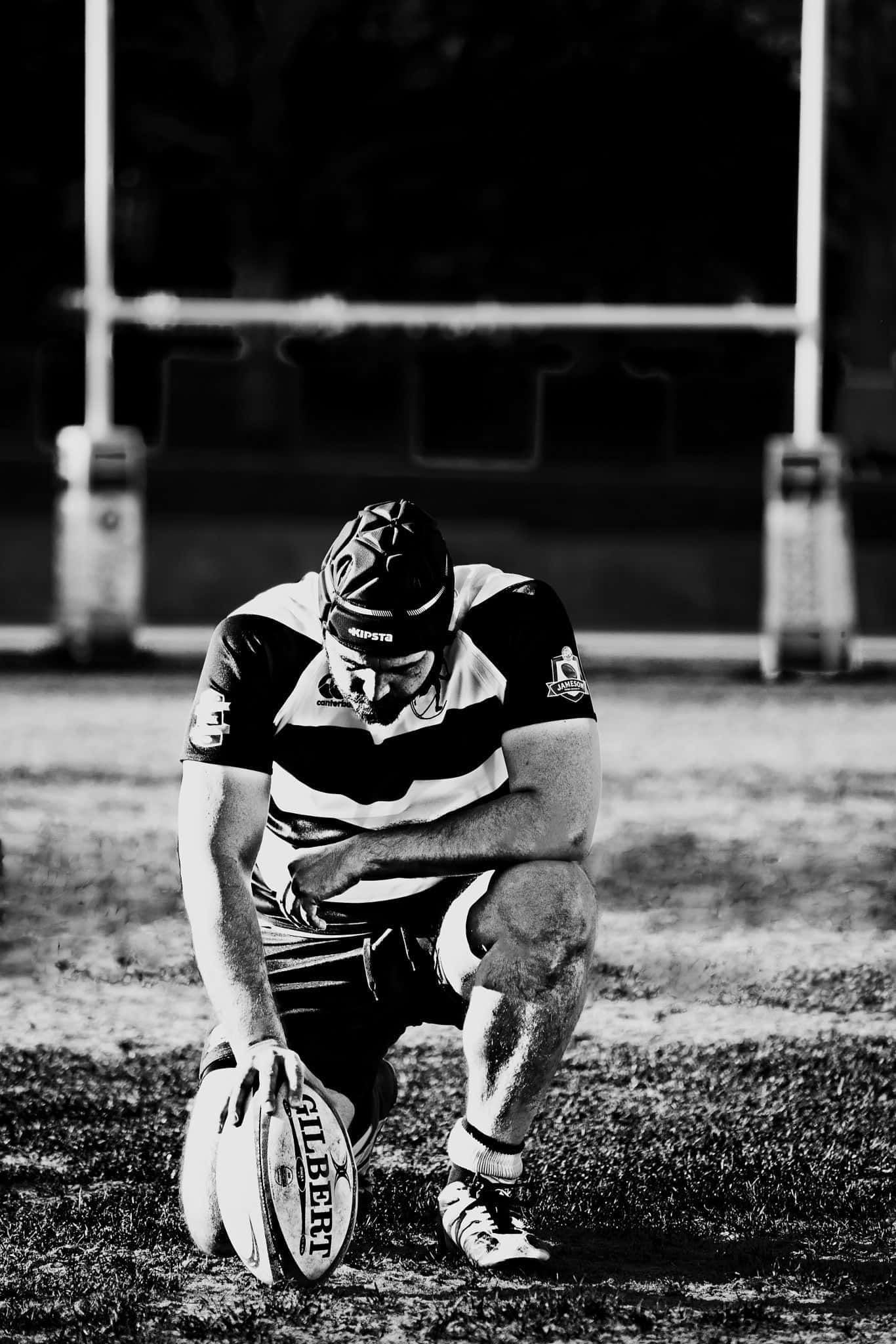Scotland Rugby 桌布 壁紙 — 一張黑白照片，一名橄欖球運動員跪在草地上，低頭抱球，顯得筋疲力盡。