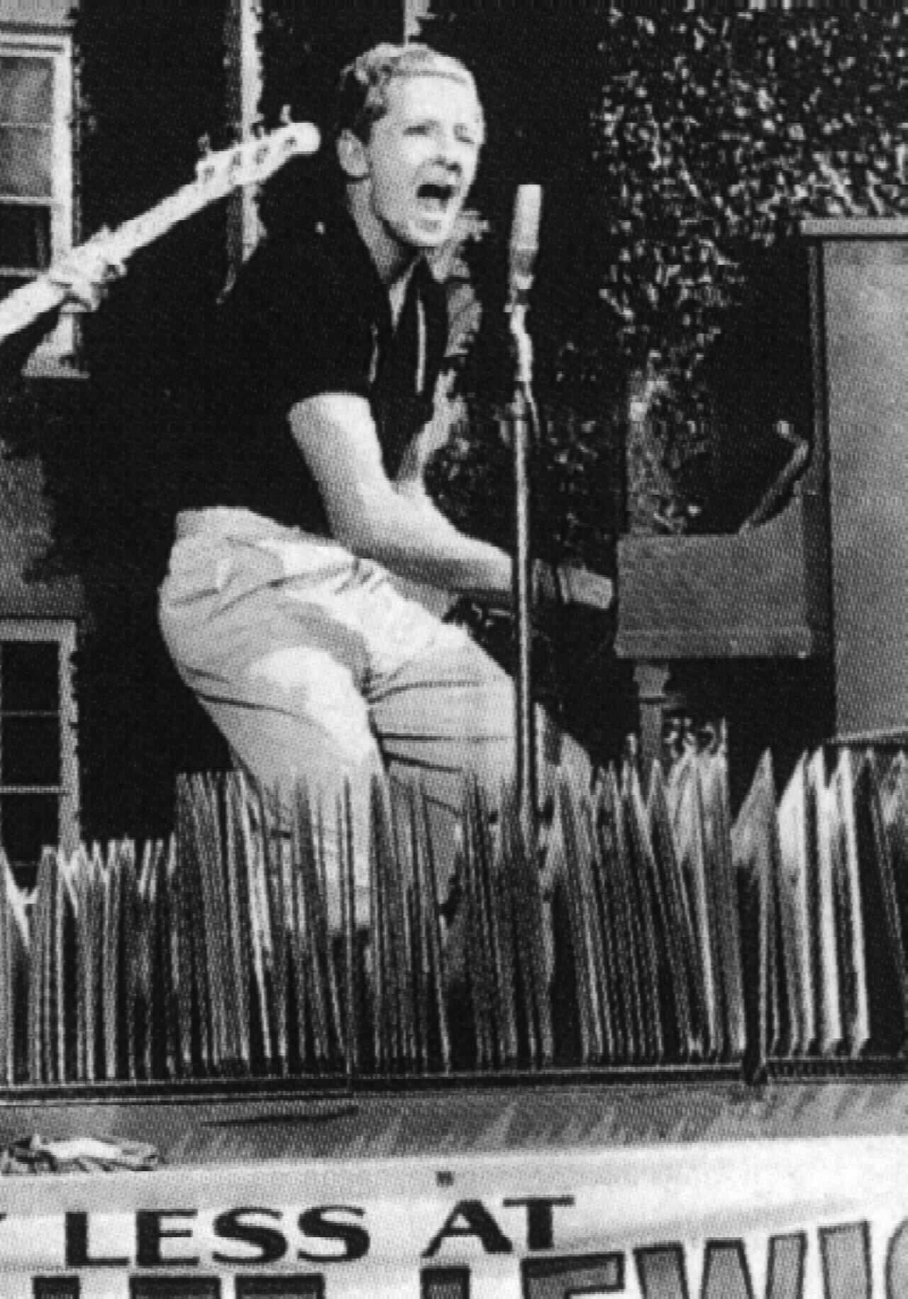 Jerry Lee Lewis 桌布 壁紙 — 一張黑白照片，一名男子在舞台上對著復古麥克風熱情歌唱，身後有鋼琴和吉他。