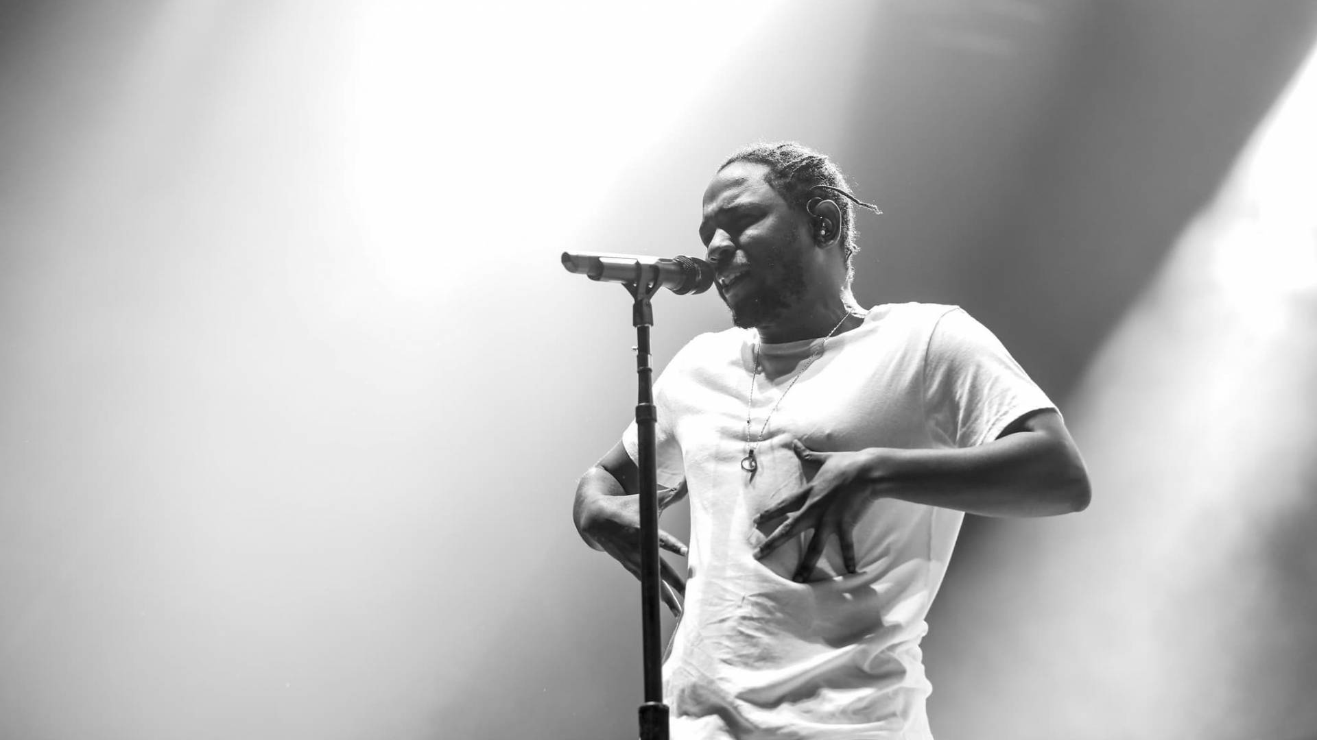 Kendrick 桌布 壁紙 — 一張黑白照片，一名男歌手在戲劇性的聚光燈下拿著麥克風在舞台上表演。