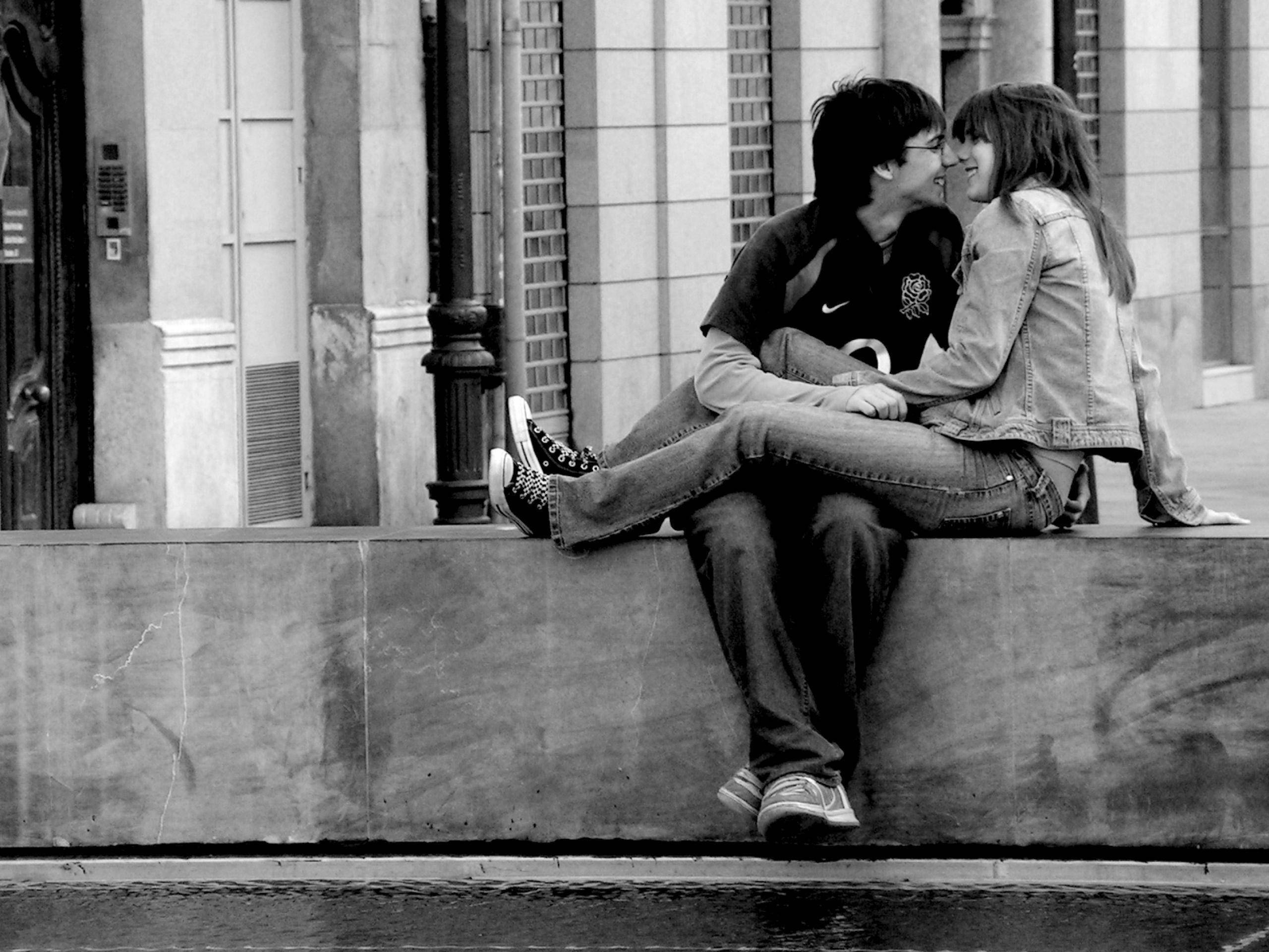 Romantic Love 桌布 壁紙 — 一張黑白照片，一對年輕情侶在都市環境中緊靠著坐在石台上，分享親密時刻。
