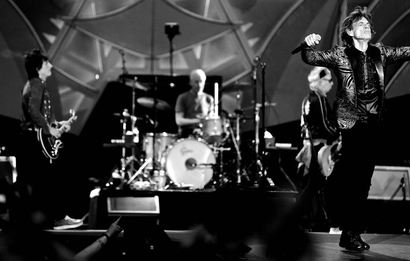 Rock 桌布 壁紙 — 一張黑白照片，一支搖滾樂團在舞台上表演，主唱穿著閃亮夾克，熱情地做手勢。