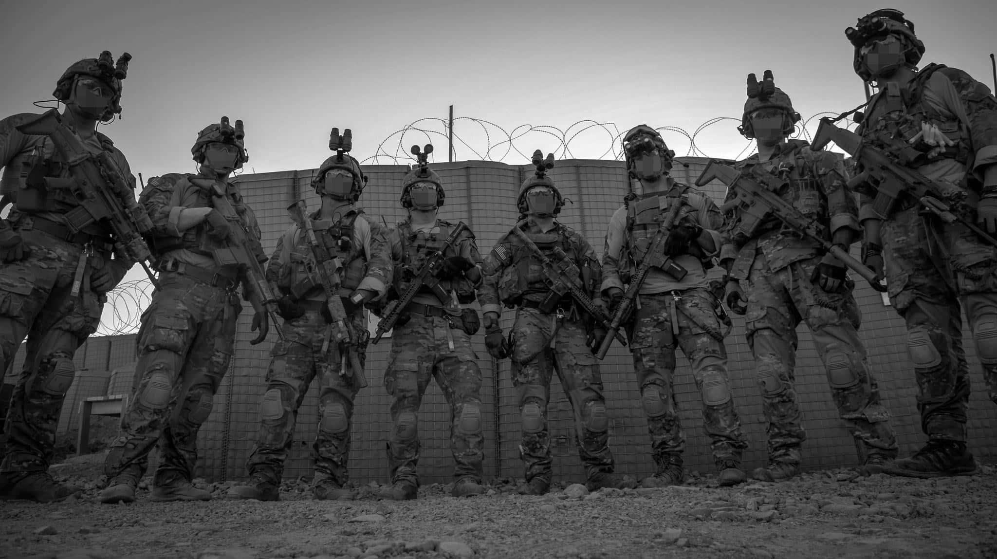 軍事動圖 桌布 壁紙 — 一張黑白照片，七名全副武裝的士兵排成一排，站在帶有鐵絲網的圍欄前。