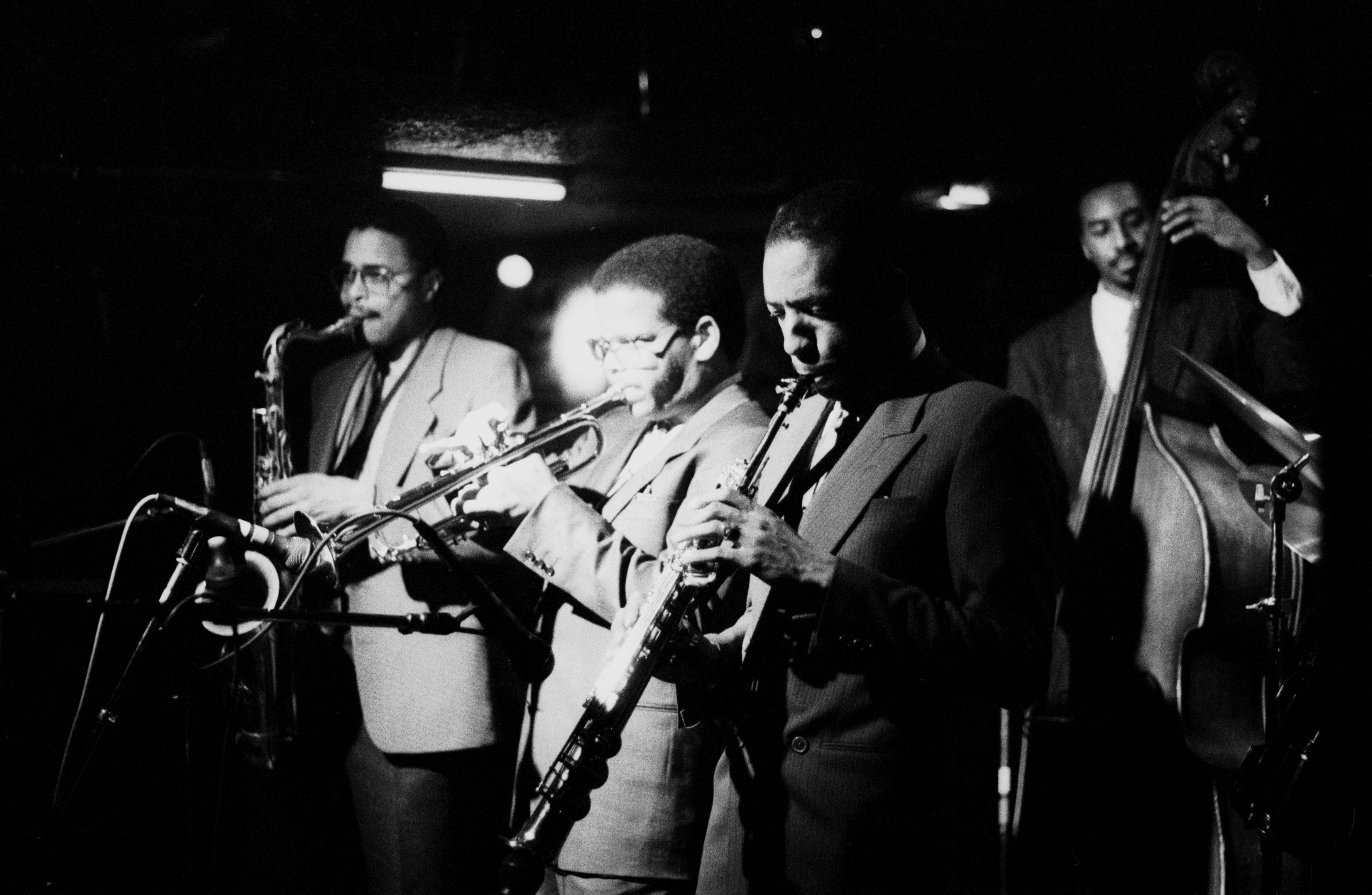 Jazz 桌布 壁紙 — 一張黑白照片，四位爵士樂手在昏暗燈光下於舞台上表演，配有麥克風和樂器。