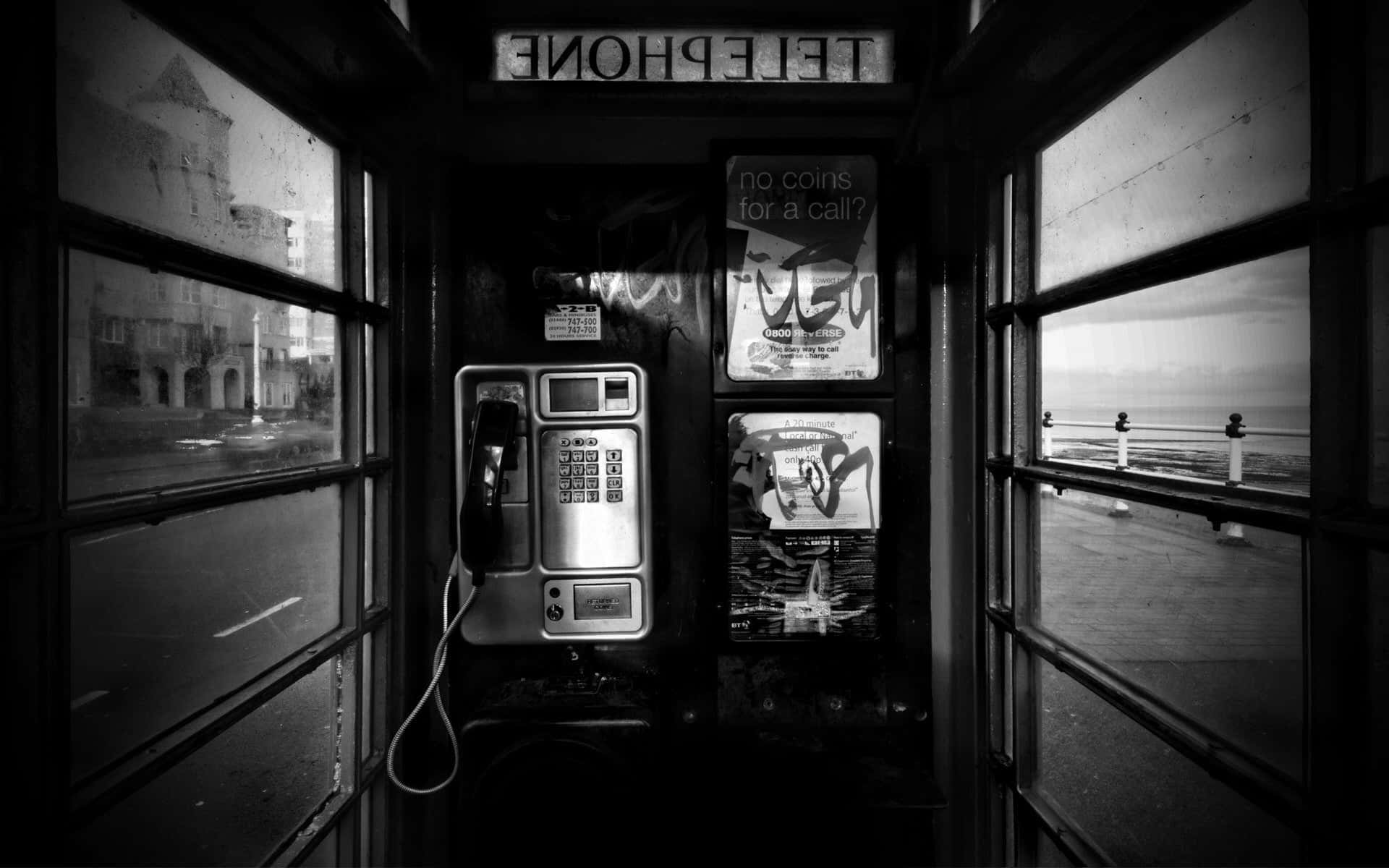 Black And White City 桌布 壁紙 — 一張黑白照片，展示了一個帶有塗鴉海報的復古電話亭，以及透過雨痕斑斑的窗戶看到的碼頭景色。