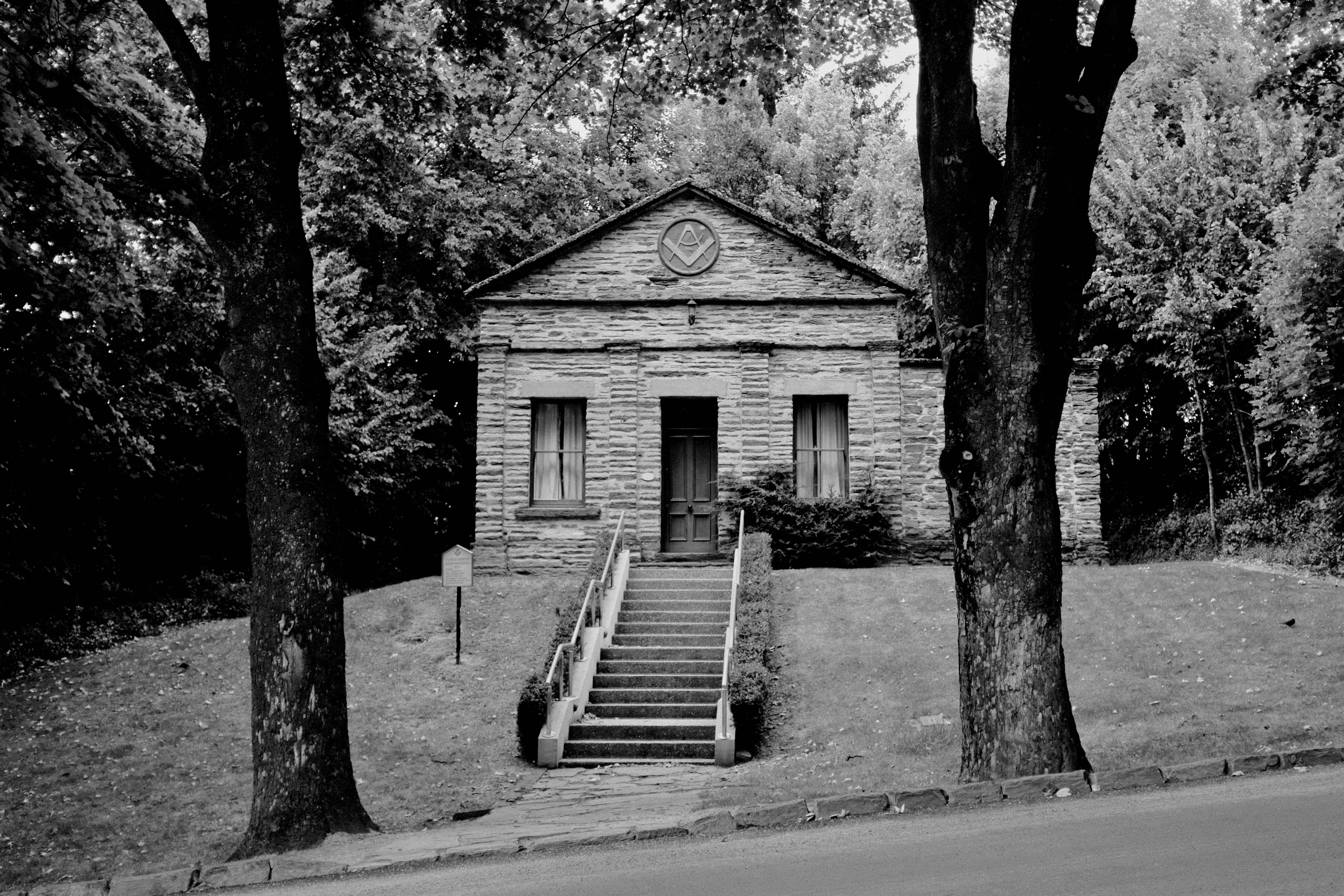 Masonic 桌布 壁紙 — 一張黑白照片，展示了一座石造共濟會會所建築，四周環繞著高大的樹木，並有樓梯通往入口。
