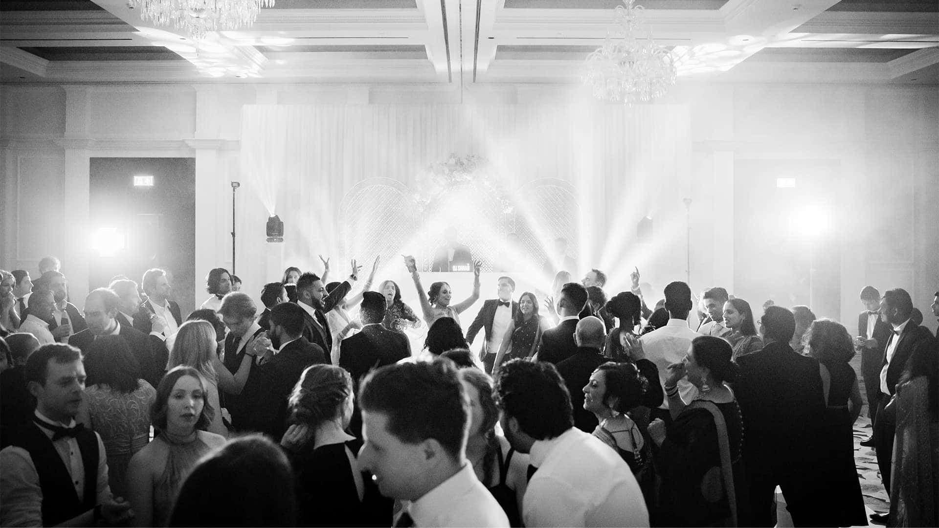 Bride And Groom 桌布 壁紙 — 一張黑白照片，展示在宏偉大廳中，賓客在明亮聚光燈下跳舞的熱鬧婚宴。