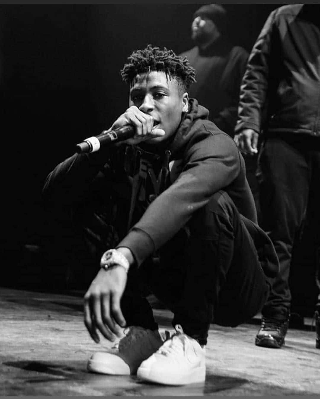 Youngboy Never Broke Again 桌布 壁紙 — 一張黑白照片，年輕饒舌歌手蹲在舞台上，專注地握著麥克風。