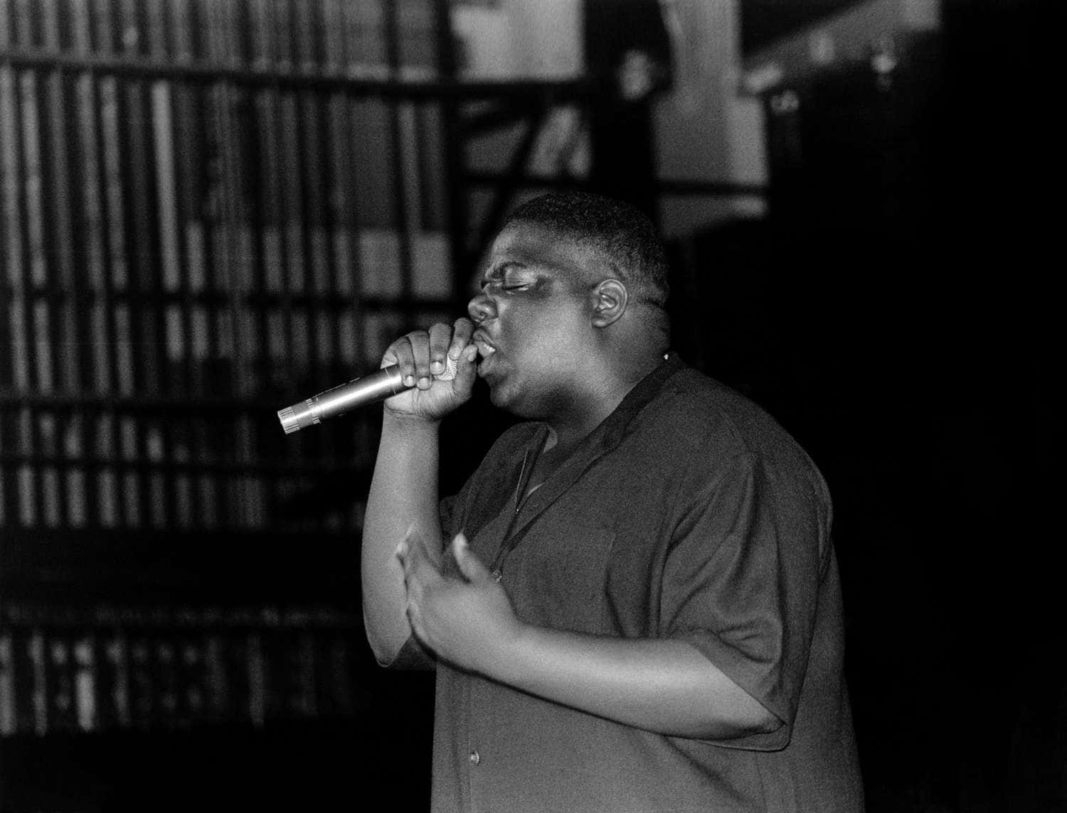 hiphop 桌布 壁紙 — 一張黑白照片，拍攝一名男子在燈光昏暗的舞台上，背景有書架，他正充滿激情地對著麥克風唱歌。