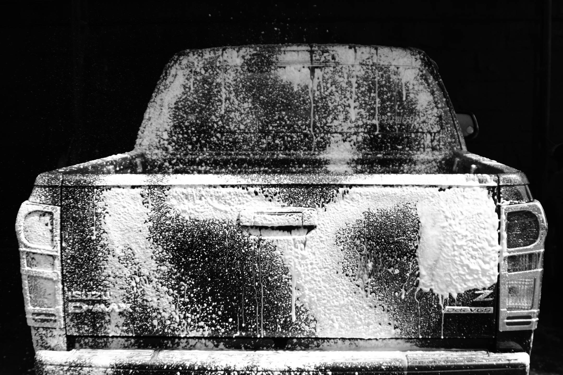 Wash 桌布 壁紙 — 一張黑白照片，拍攝一輛皮卡車的後部，覆蓋著厚厚的肥皂泡沫，背景為深色。