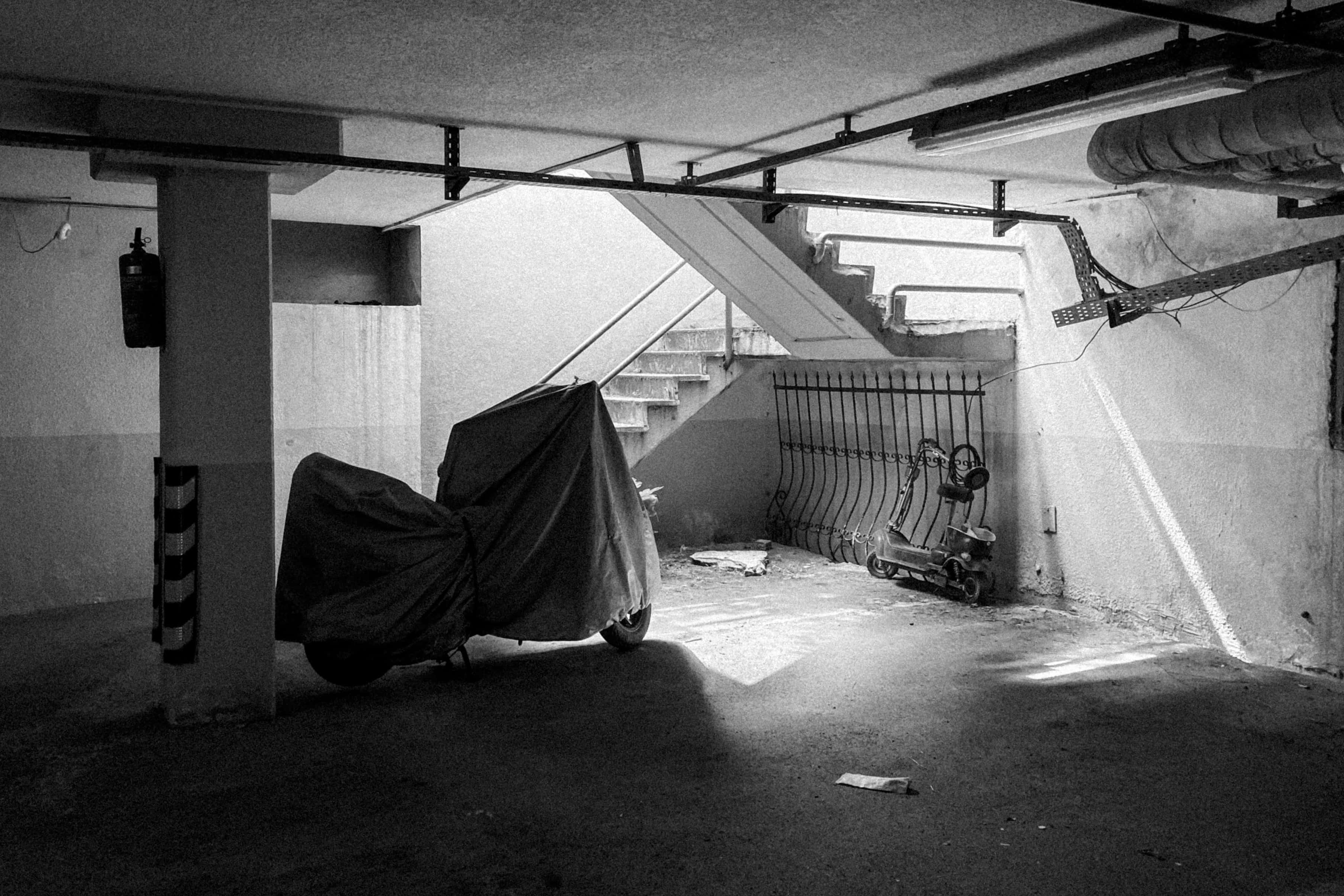 Underground 桌布 壁紙 — 一張黑白照片，拍攝了有蓋和無蓋的滑板車在光線昏暗的地下停車場，有混凝土柱和樓梯。