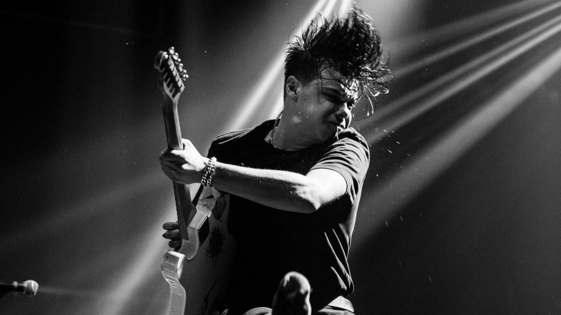 head banging 桌布 壁紙 — 一張黑白照片，捕捉一位吉他手在表演中，帶有刺蝟頭和舞台燈光劃破空氣的瞬間。