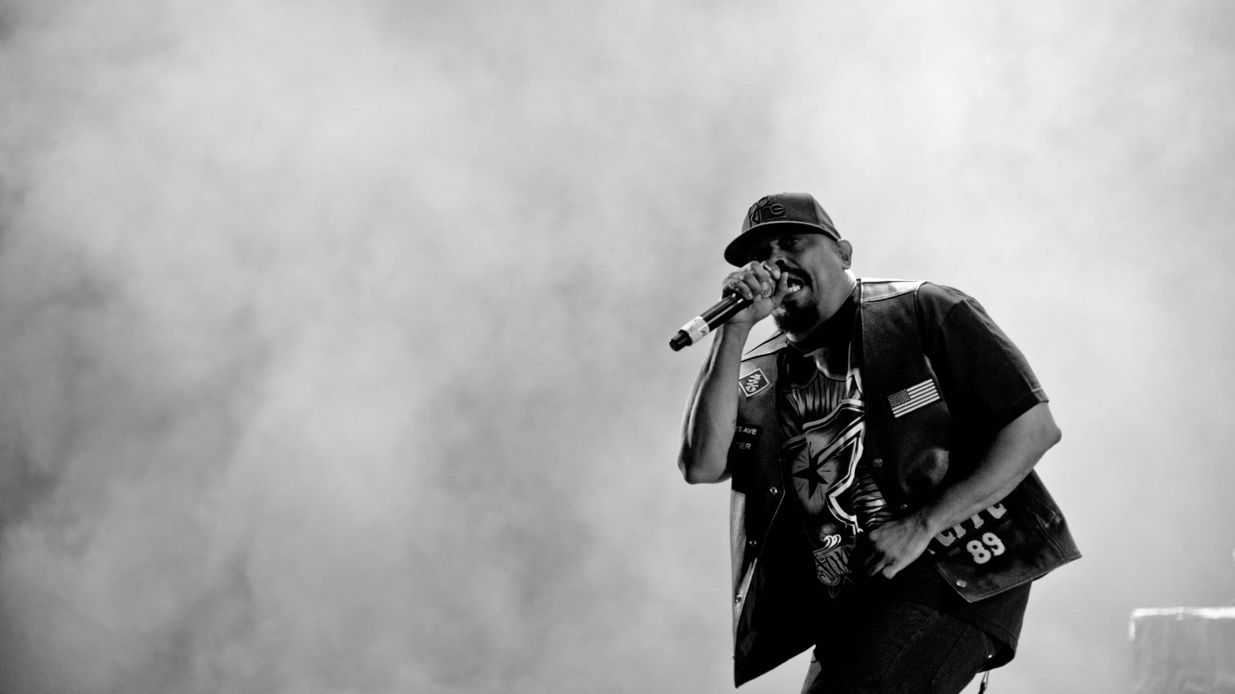 4K Rapper 桌布 壁紙 — 一張黑白照片，捕捉到一位饒舌歌手在舞台煙霧繚繞中，熱情地對著麥克風演唱。