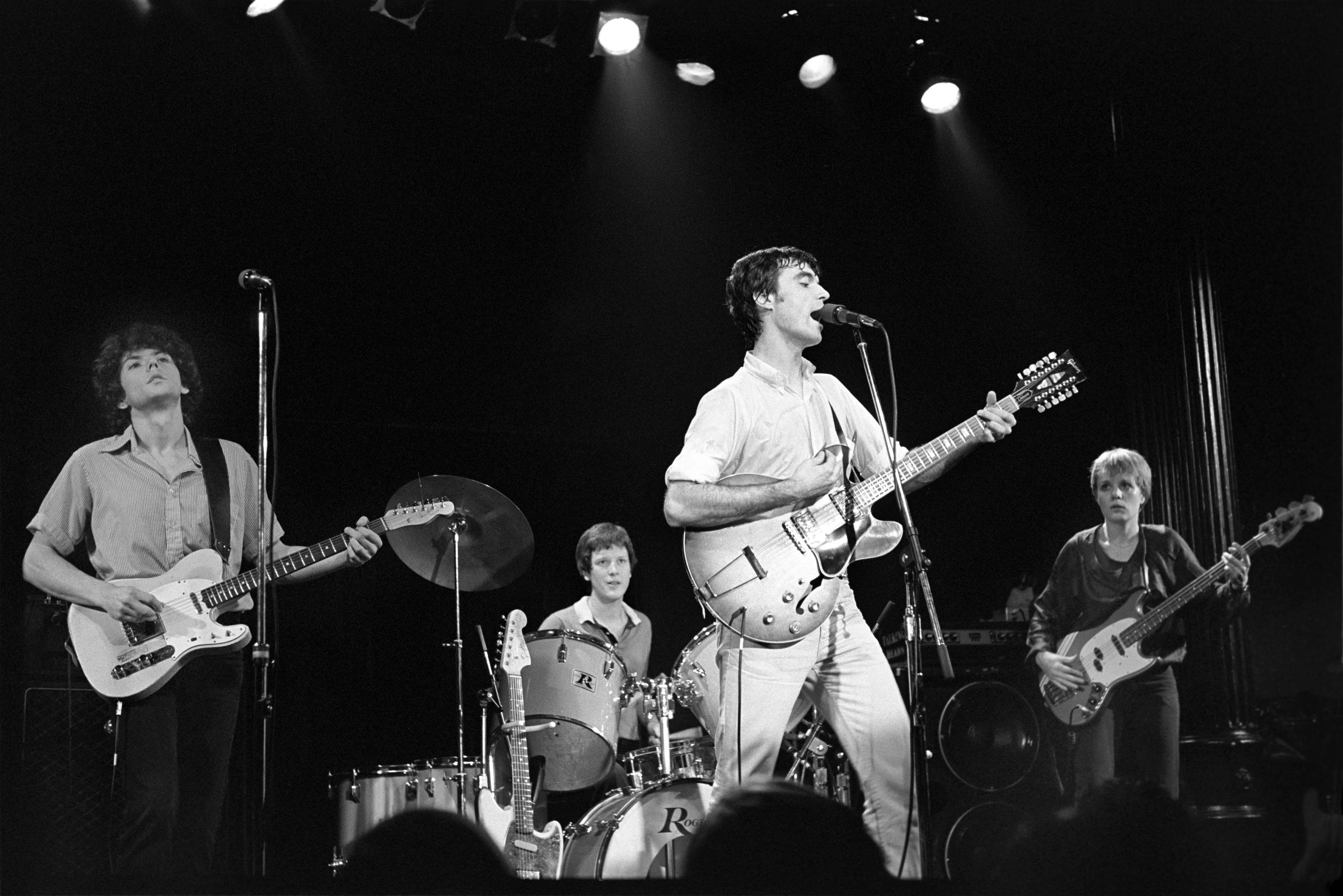 band 桌布 壁紙 — 一張黑白照片，搖滾樂團在明亮的聚光燈下現場表演，前景有觀眾剪影。