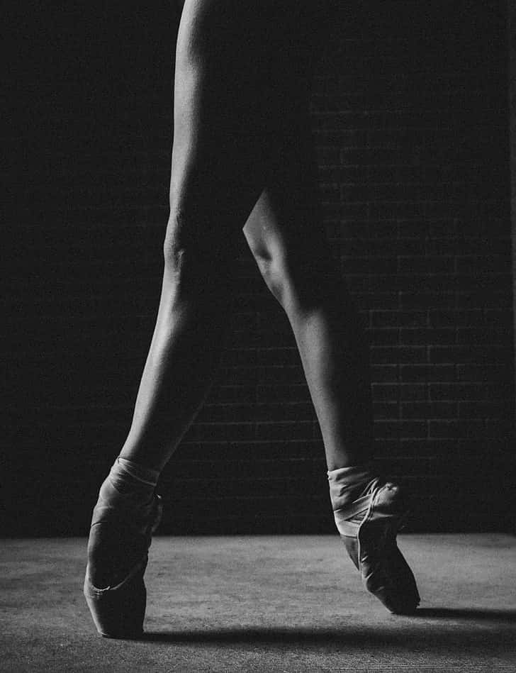 ballerina 桌布 壁紙 — 一張黑白照片，芭蕾舞者的雙腿以足尖姿勢立於深色磚牆前。