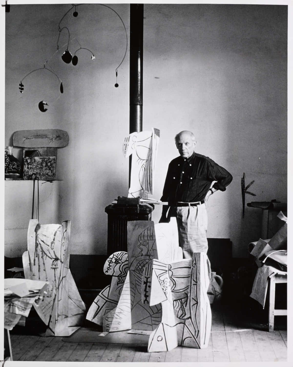 Picasso 桌布 壁紙 — 一張黑白照片，藝術家亞歷山大·考爾德自信地站在他雜亂的工作室中，周圍環繞著他的動態雕塑和大型紙張剪裁。