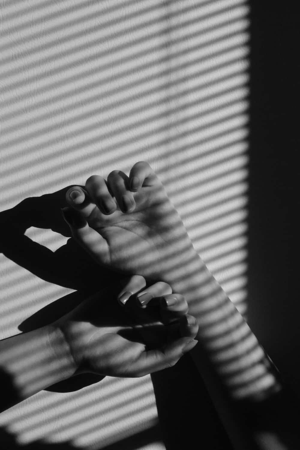 hands 桌布 壁紙 — 一張黑白照片，雙手輕輕托著一隻腳，靠在條紋窗簾上，投射出戲劇性的陰影。