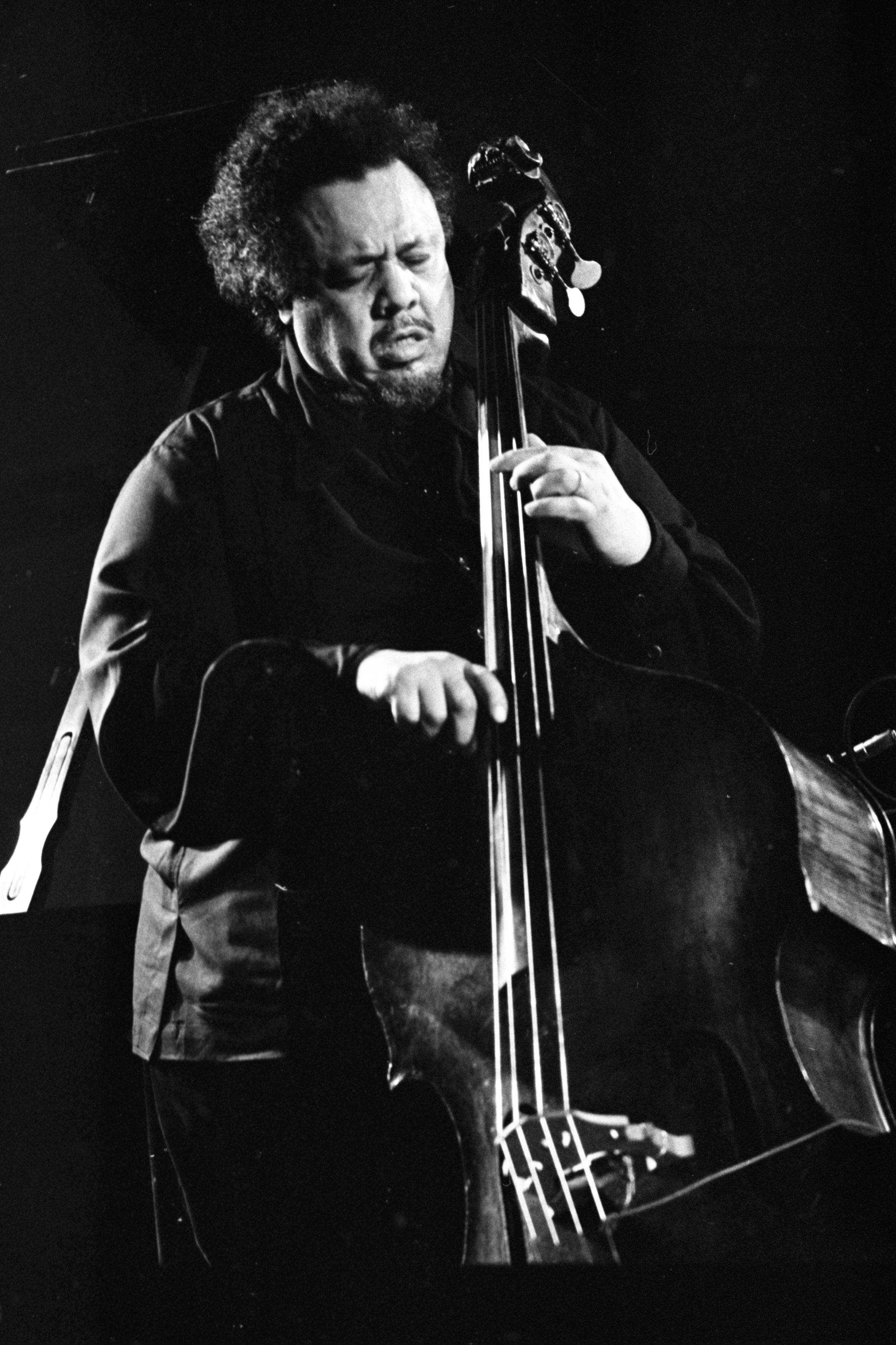 Charles Mingus 深情彈奏貝斯吉他 壁紙 — 一張黑白照片，音樂家在戲劇性的舞台燈光下激烈地演奏低音大提琴。