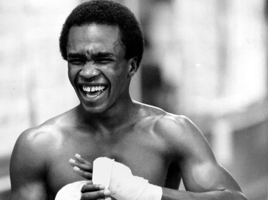 Boxing 桌布 壁紙 — 一張黑白照片，顯示一位肌肉發達的拳擊手，開心大笑，同時舉起包紮好的雙手。