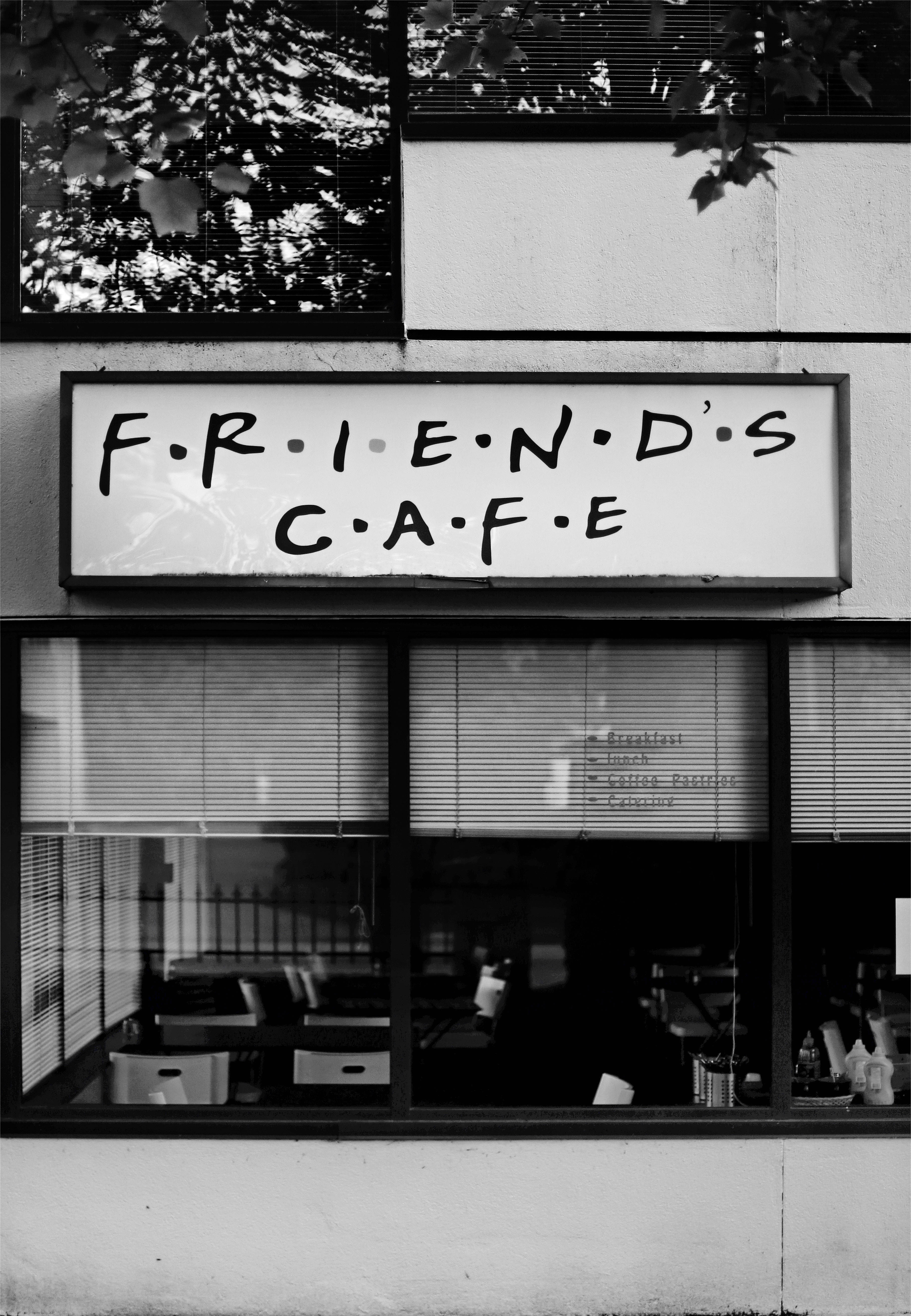 Friends 桌布 壁紙 — 一張黑白照片，顯示一個寫著FRIEND'S CAFE的咖啡館招牌，頂部有樹葉框住。