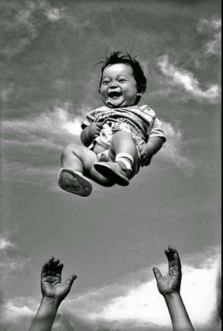 smiling 桌布 壁紙 — 一張黑白照片中，一個快樂的嬰兒在半空中大笑，下方有雙手伸向天空，背景是陰天。