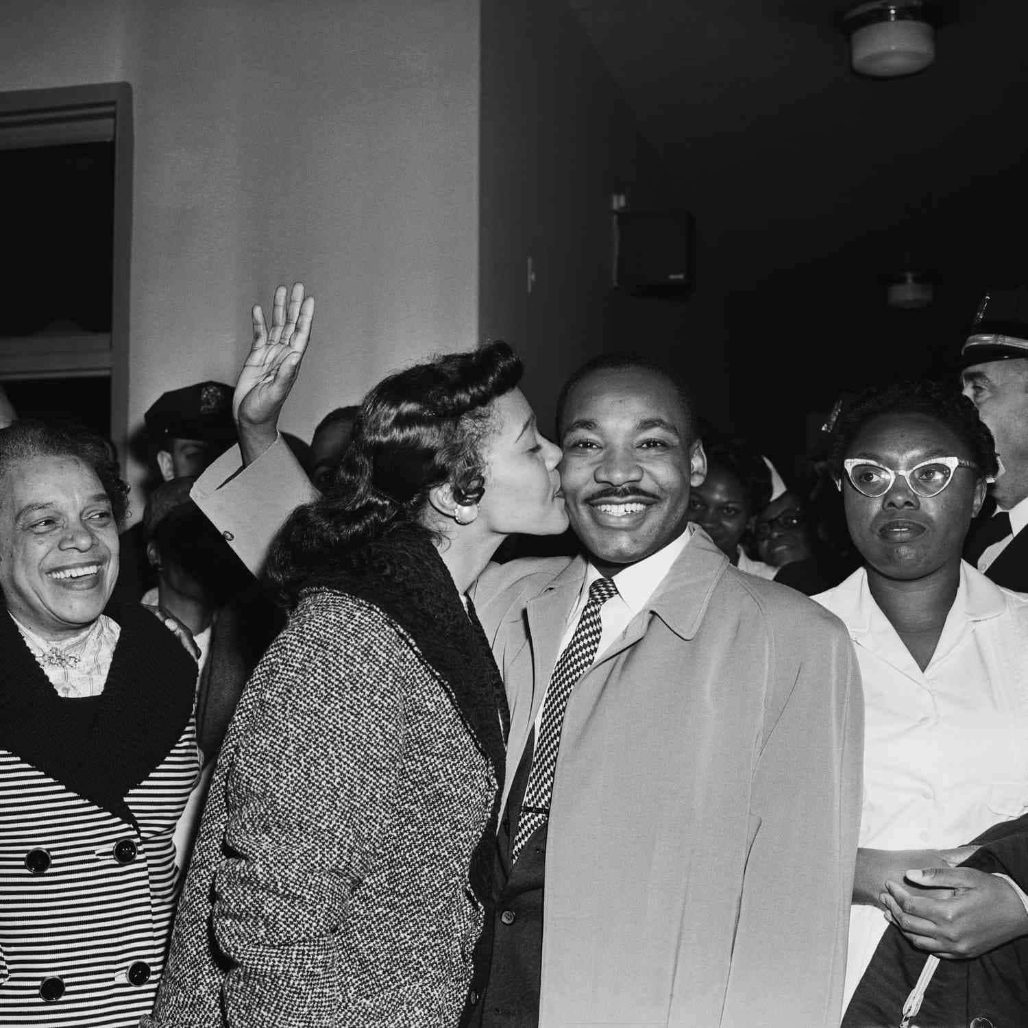 Black Couple 桌布 壁紙 — 一張黑白照片捕捉了一個歡樂的時刻，一名女子在擁擠的室內環境中微笑著親吻馬丁·路德·金恩博士的臉頰。