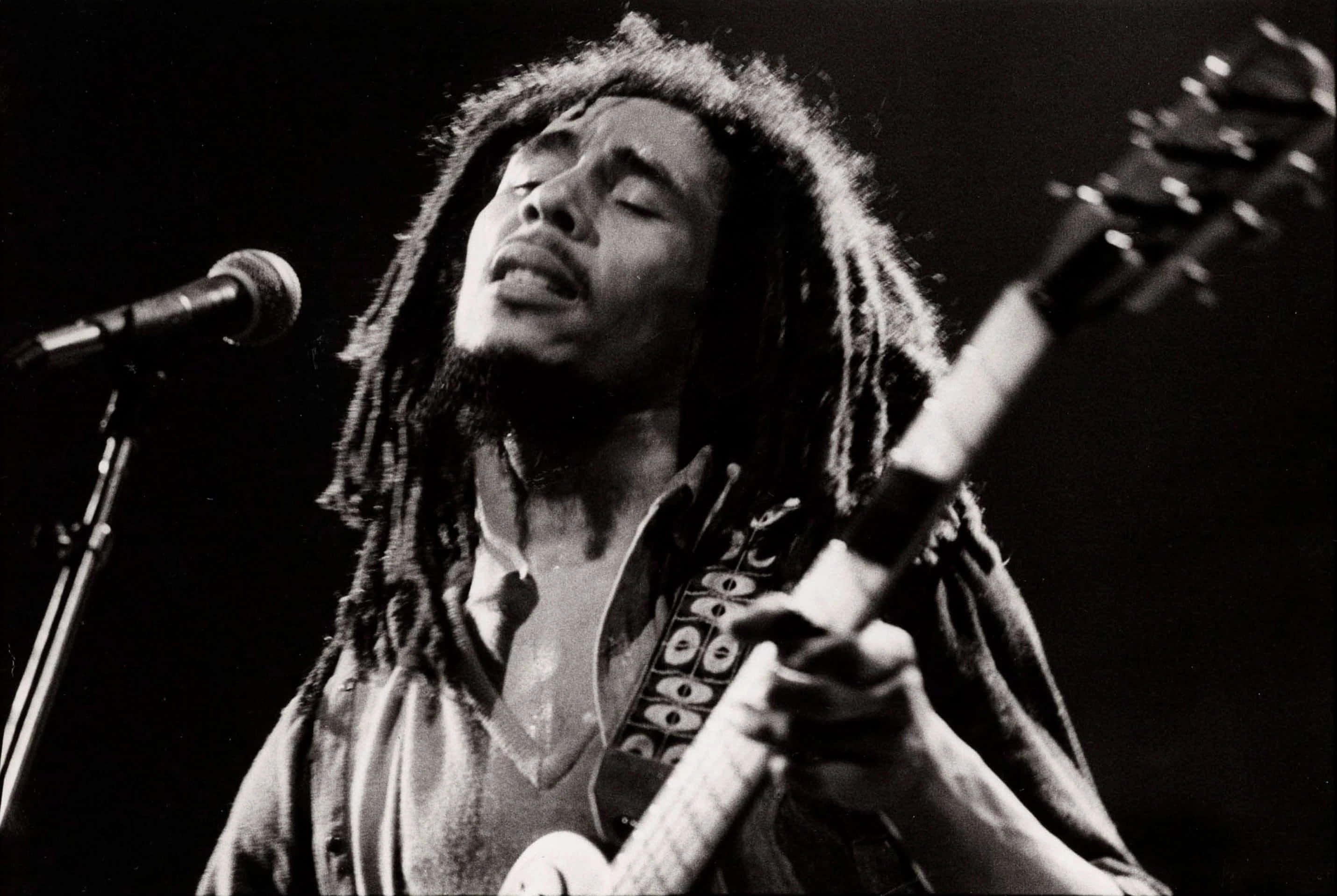 Bob Marley 桌布 壁紙 — 一張黑白照片捕捉到 Bob Marley 閉著眼睛，一邊彈吉他一邊充滿激情地對著麥克風唱歌。