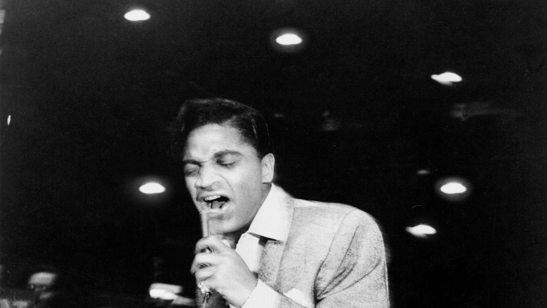 Singer 桌布 壁紙 — 一張黑白照片捕捉到一位充滿激情的男歌手在舞台燈光下拿著麥克風表演的瞬間。