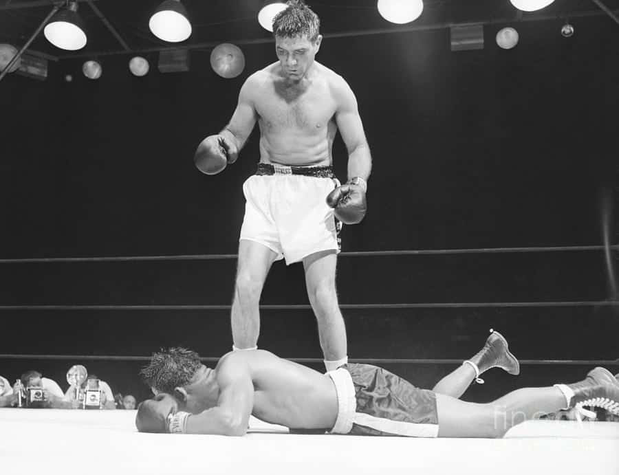 Boxing 桌布 壁紙 — 一張黑白照片捕捉到一位勝利的拳擊手站在擂台上，俯視著倒下的對手，頭頂燈光耀眼。