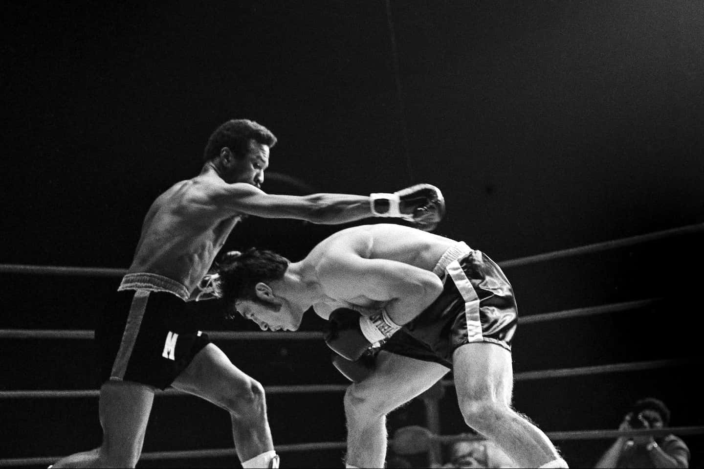 boxer 桌布 壁紙 — 一張黑白照片捕捉到一名拳擊手在燈光昏暗的擂台上向對手打出強力一拳。