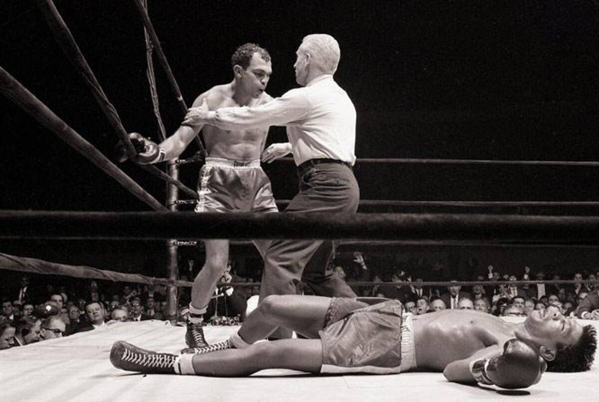 Boxing 桌布 壁紙 — 一張黑白照片捕捉到一名拳擊手站在擂台上倒下的對手旁邊，裁判正在檢查他的狀況。