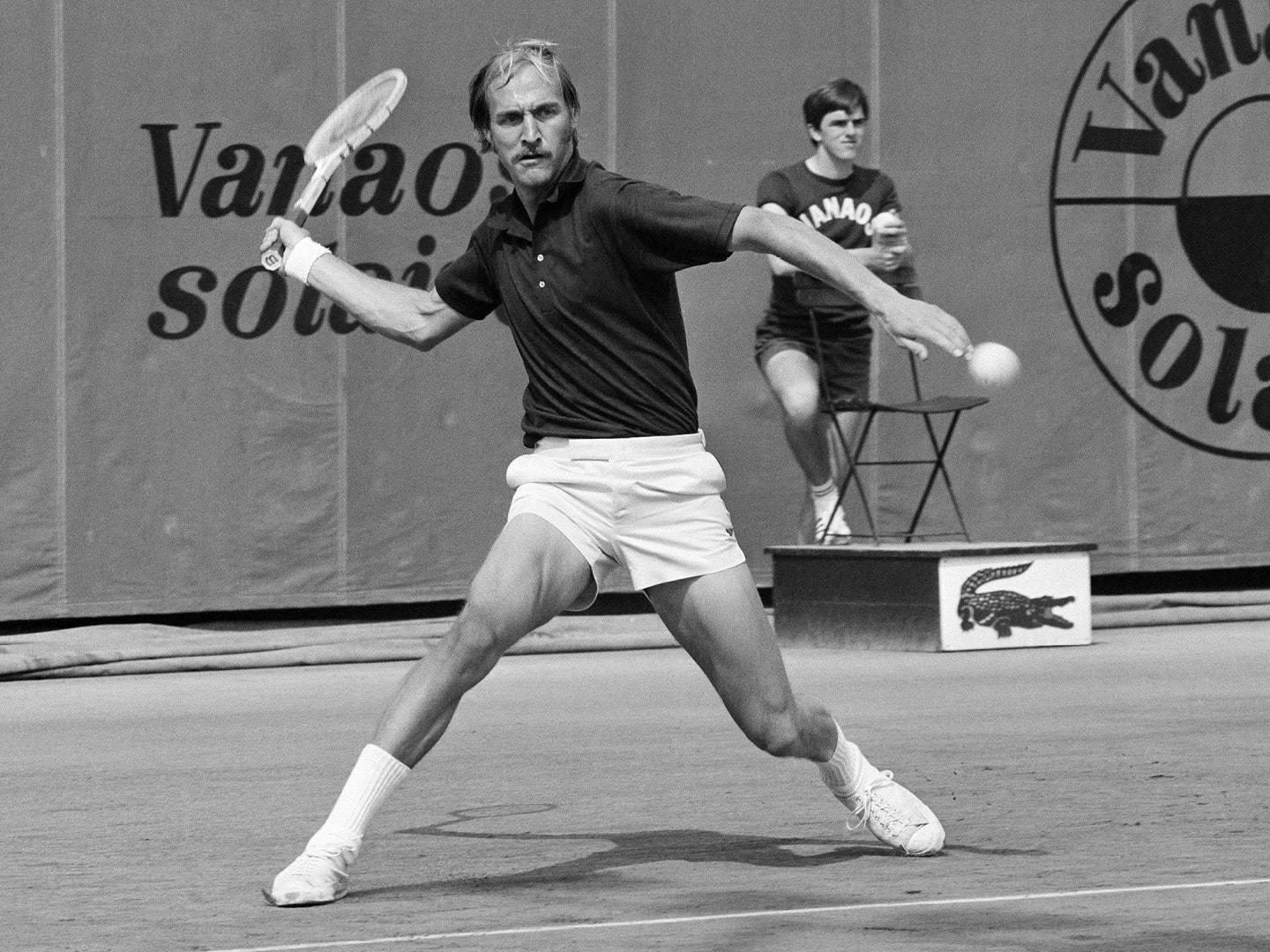 Tennis 桌布 壁紙 — 一張黑白照片捕捉到一名男網球選手在球場上揮拍擊球，球正在移動，背景中有一名坐著的球童。