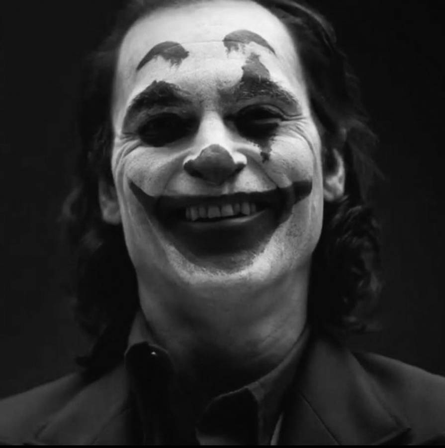 Black And White Joker 桌布 壁紙 — 一張黑白特寫，一名男子塗抹著小丑化妝，在黑暗背景中咧嘴大笑。