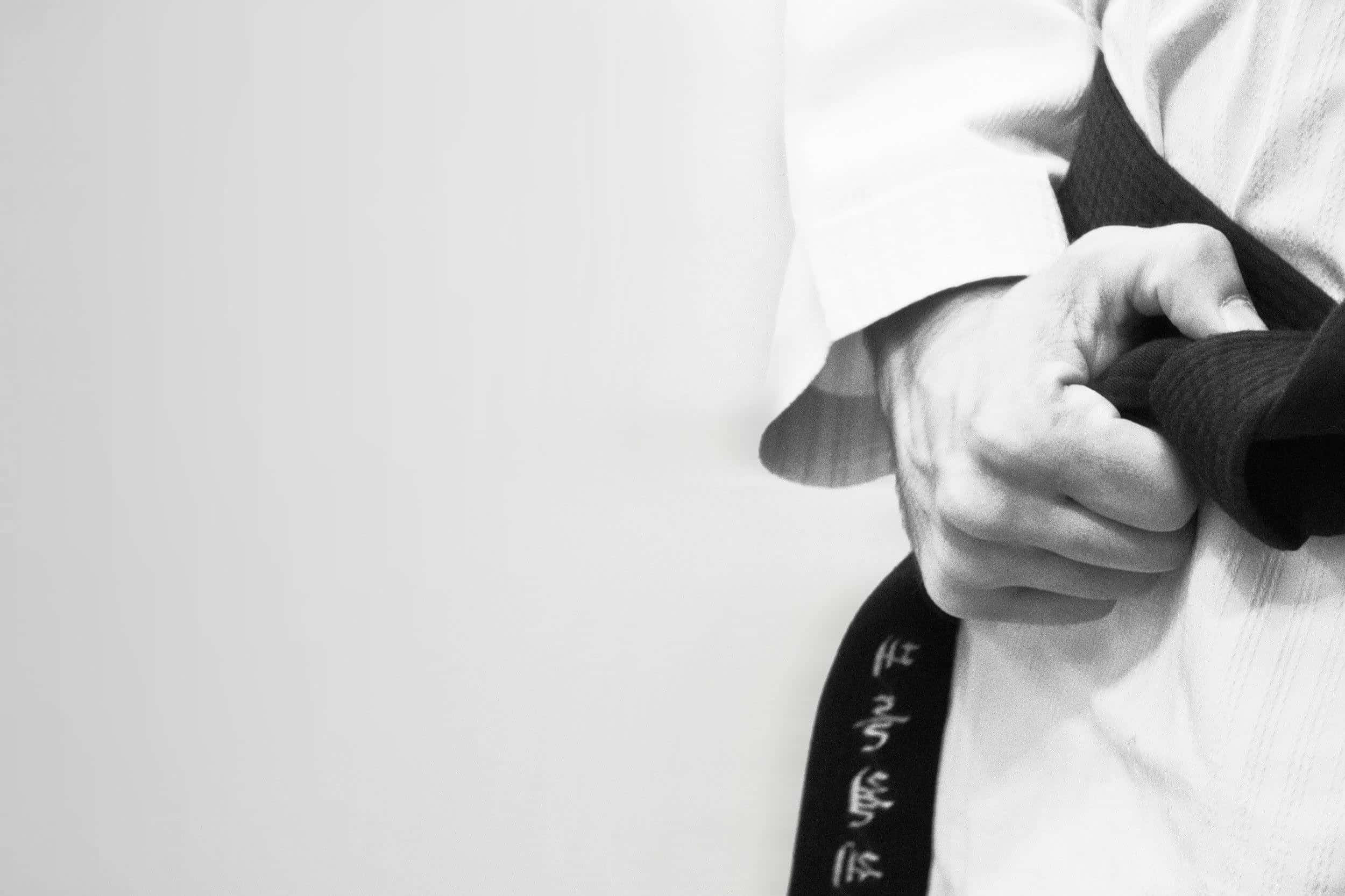 Martial Arts Uniform 桌布 壁紙 — 一張黑白特寫，拍攝一位武術家的手緊握一條帶有漢字圖案的黑帶，背景為純白色。