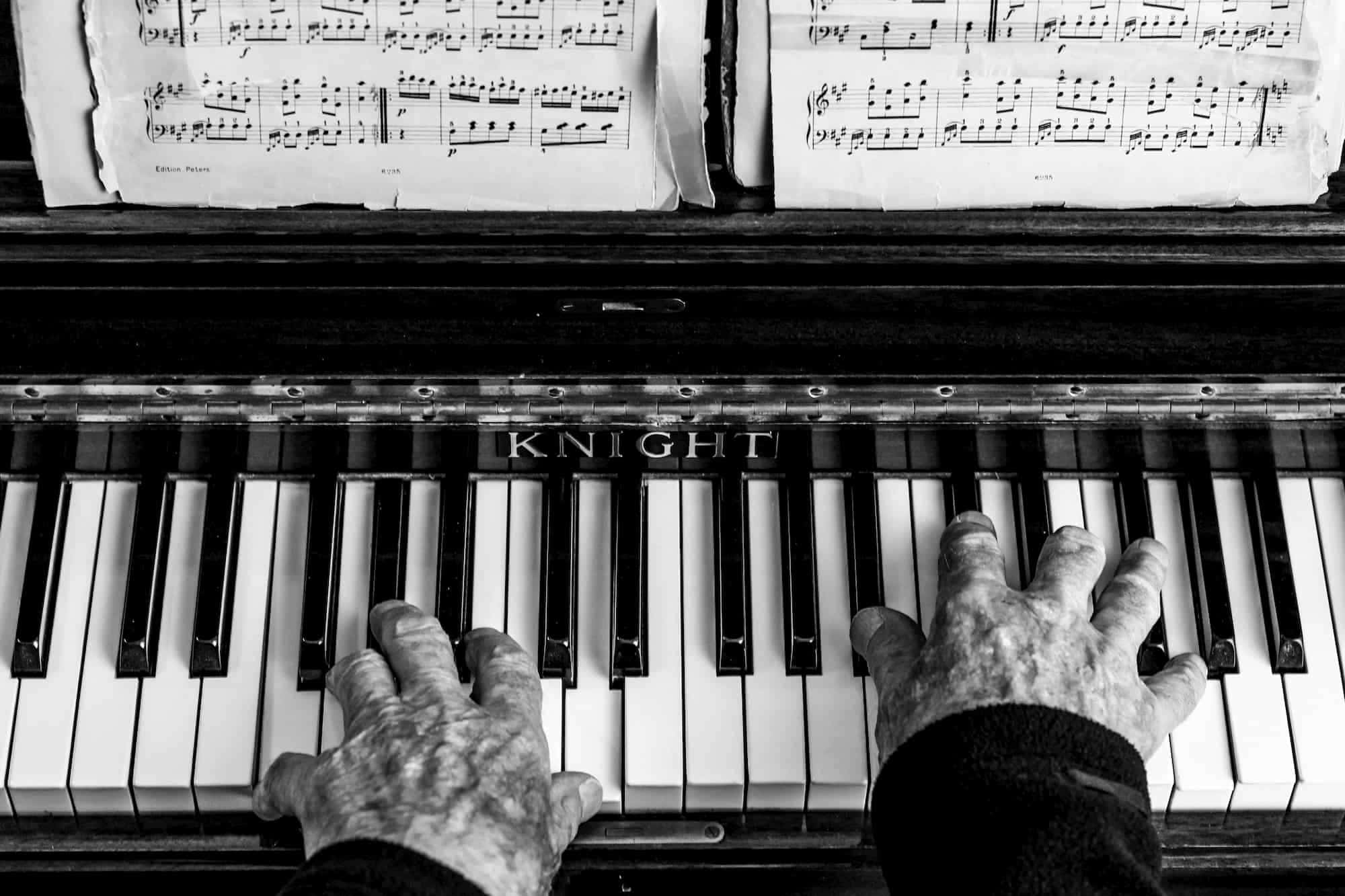 Black And White Piano 桌布 壁紙 — 一張黑白特寫，拍攝歷經風霜的手彈奏復古Knight鋼琴，上方有樂譜。