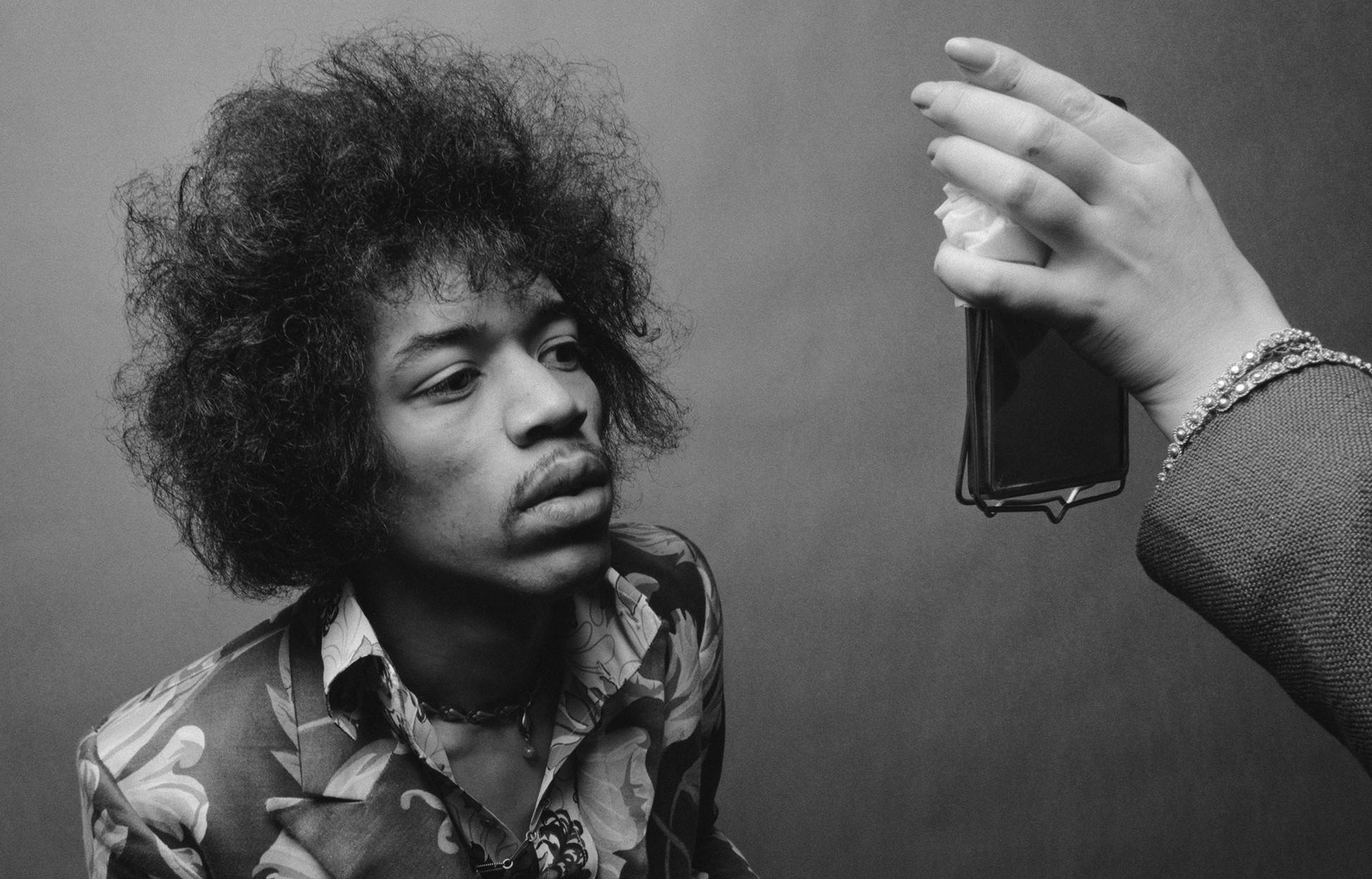 黑白 桌布 壁紙 — 一張黑白肖像，Jimi Hendrix 抬頭望向一隻在他臉旁拿著手機的手。
