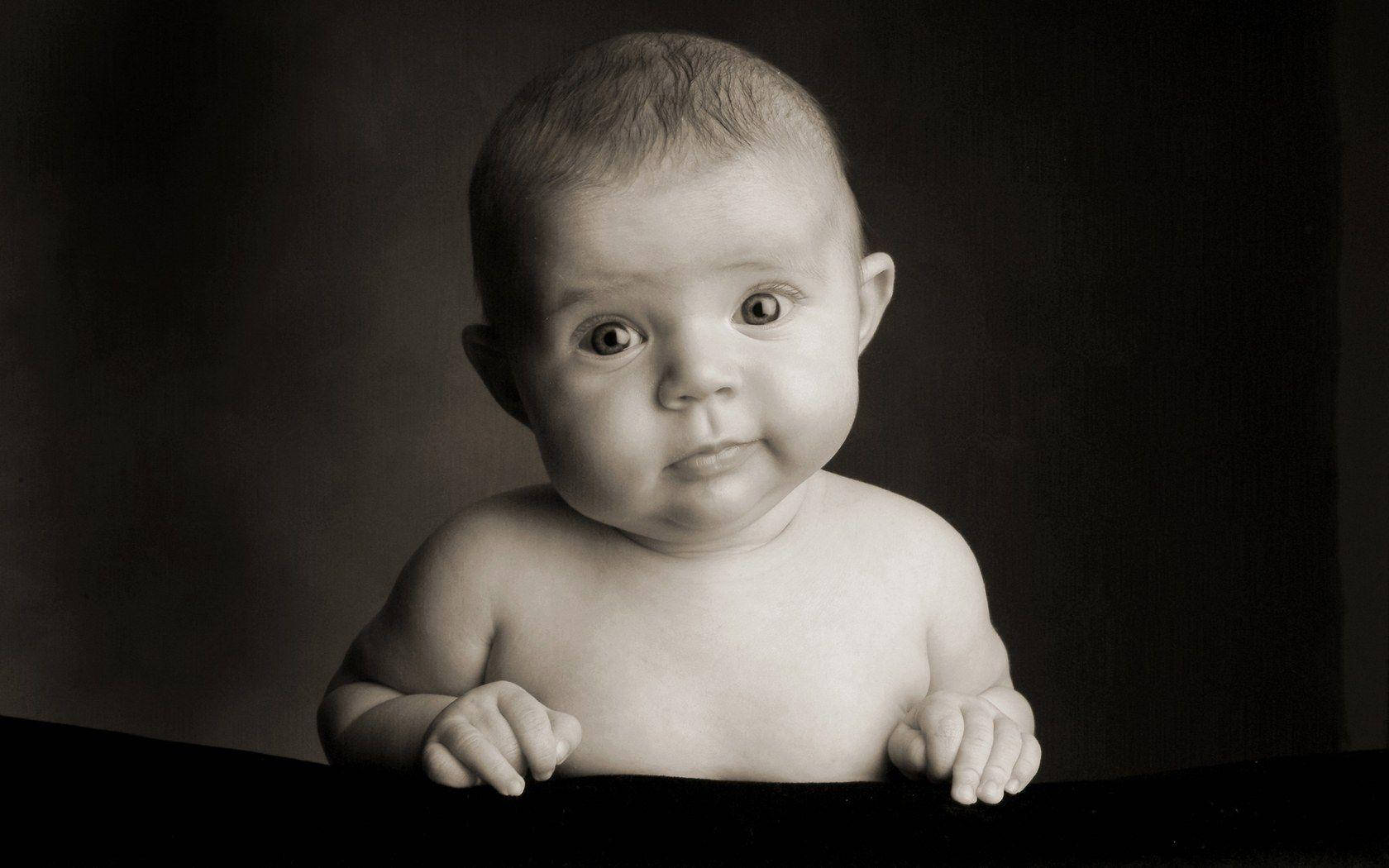 Newborn 桌布 壁紙 — 一張黑白肖像，一個嬰兒睜著好奇的大眼睛，從黑暗表面上方探出頭來。