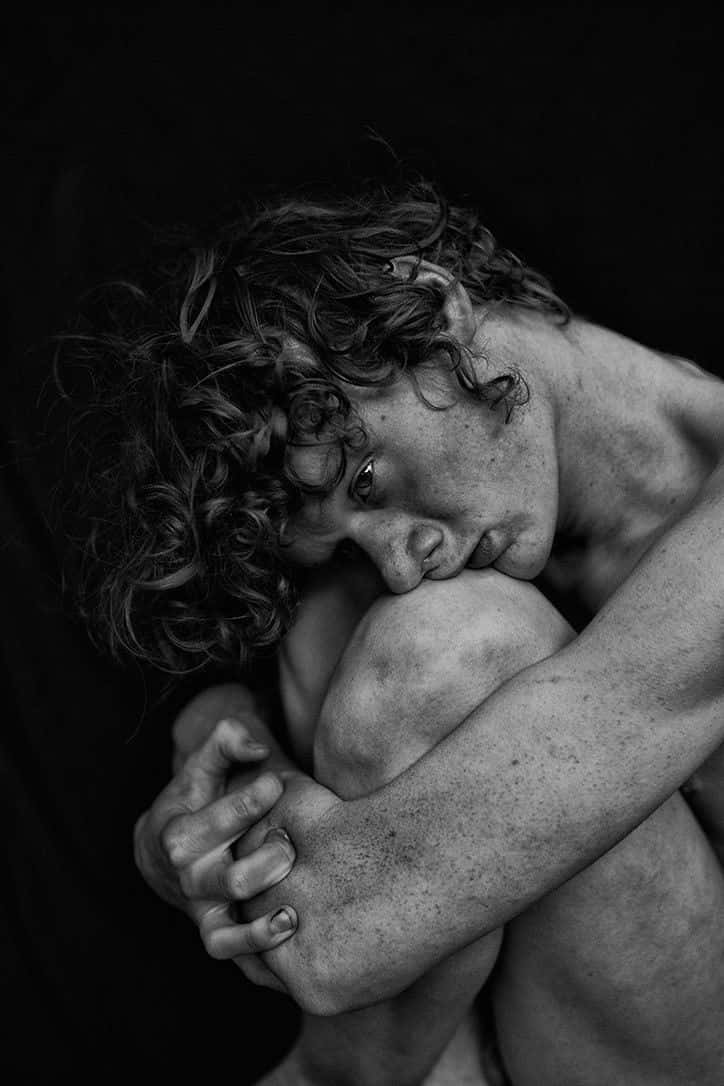 emotion 桌布 壁紙 — 一張黑白肖像，拍攝對象是捲髮人士，在深色背景前以脆弱姿勢抱膝。