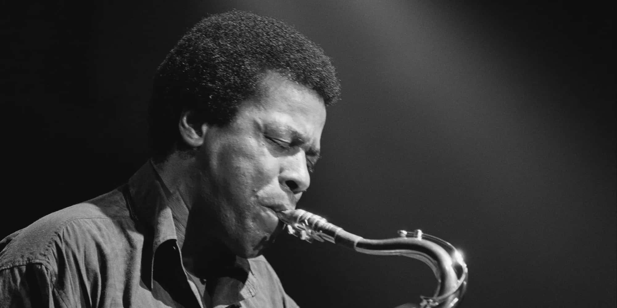 Wayne Shorter 桌布 壁紙 — 一張黑白肖像，捕捉一位爵士薩克斯風演奏家在戲劇性舞台燈光下，深深沉浸在充滿靈魂的表演中。
