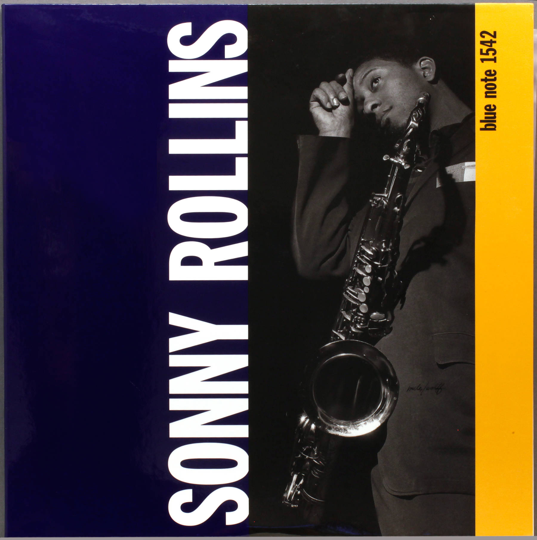 音樂 桌布 壁紙 — 一張黑白肖像，爵士薩克斯風手 Sonny Rollins 在深色背景前手持樂器，背景帶有醒目的藍色和黃色圖形元素。