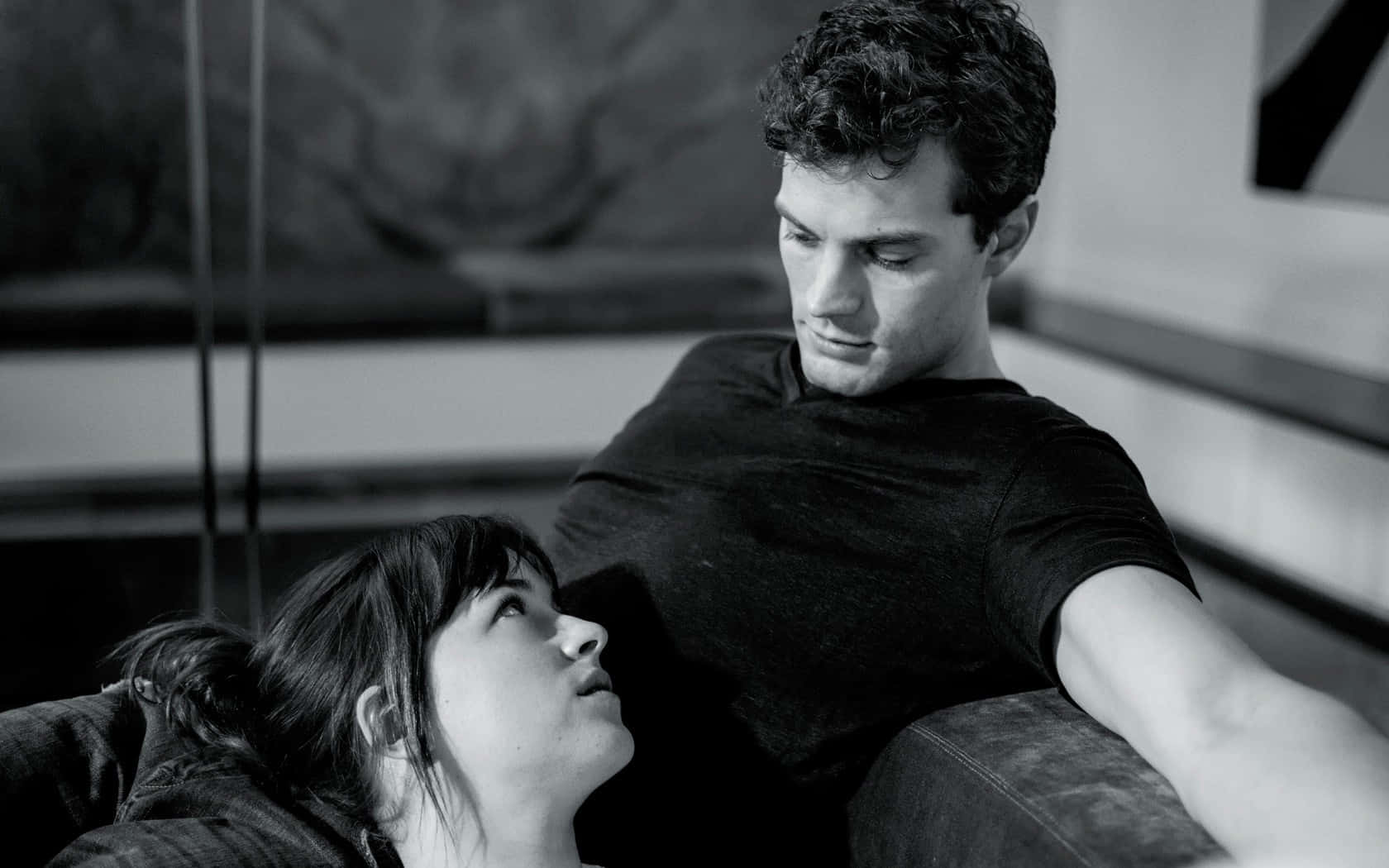 jamie dornan 桌布 壁紙 — 一張黑白親密肖像，捕捉一對男女在現代室內互相凝視的瞬間。