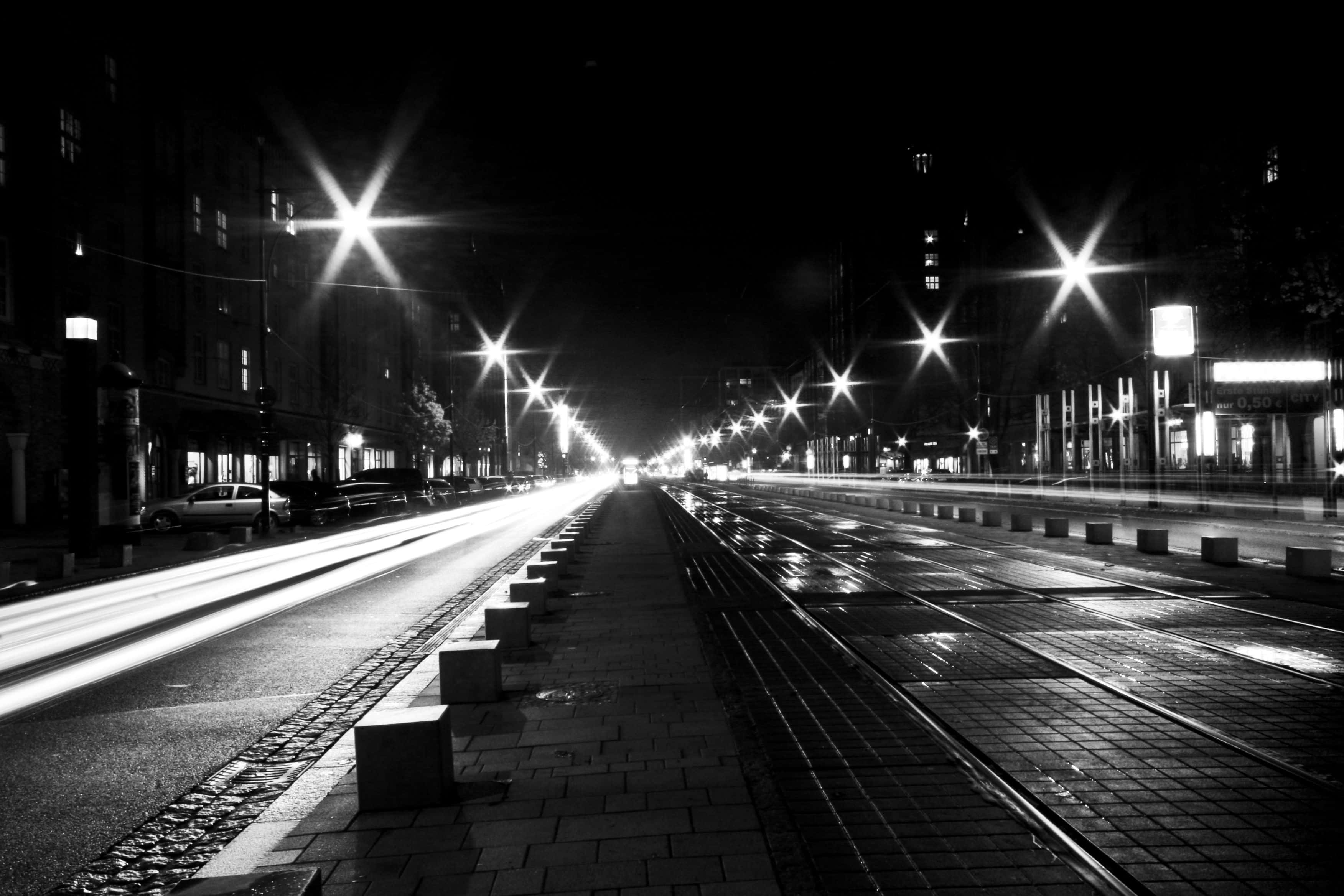 Black And White Street 桌布 壁紙 — 一張黑白長時間曝光的濕漉漉城市街道夜景，有發光的街燈和拖曳的車燈。