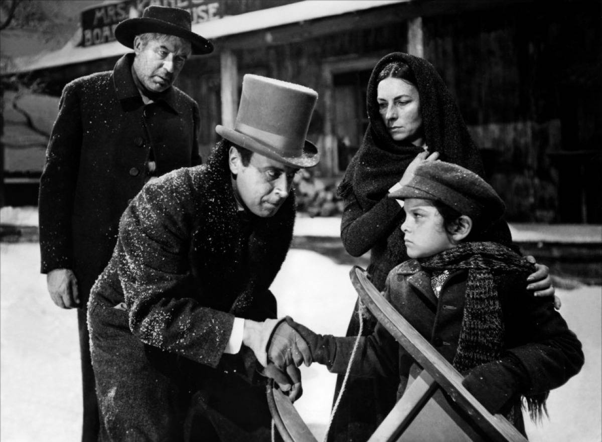 Citizen Kane 桌布 壁紙 — 一張黑白電影劇照顯示，在一個積雪的小鎮中，一名戴高帽的男子正在幫助一個孩子滑雪，而一名女子和另一名男子在旁觀看。