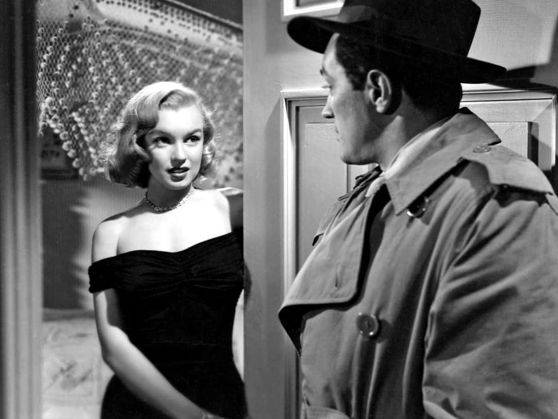 Film Noir 桌布 壁紙 — 一張黑白電影劇照顯示瑪麗蓮夢露身穿黑色連衣裙，看著一個穿著風衣和戴著軟呢帽的男人。
