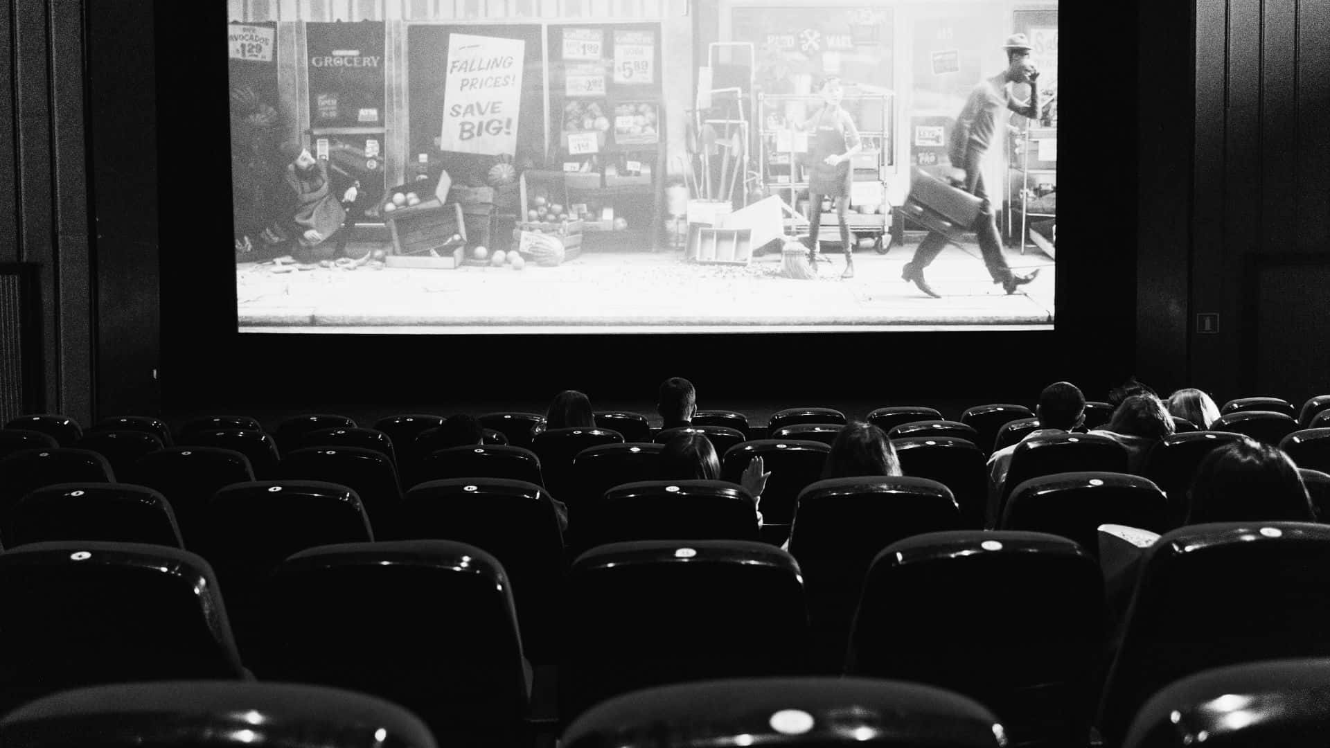 Black And White Movie 桌布 壁紙 — 一張黑白電影院照片，空座位排排面向大螢幕，螢幕上正播放黑白電影場景。