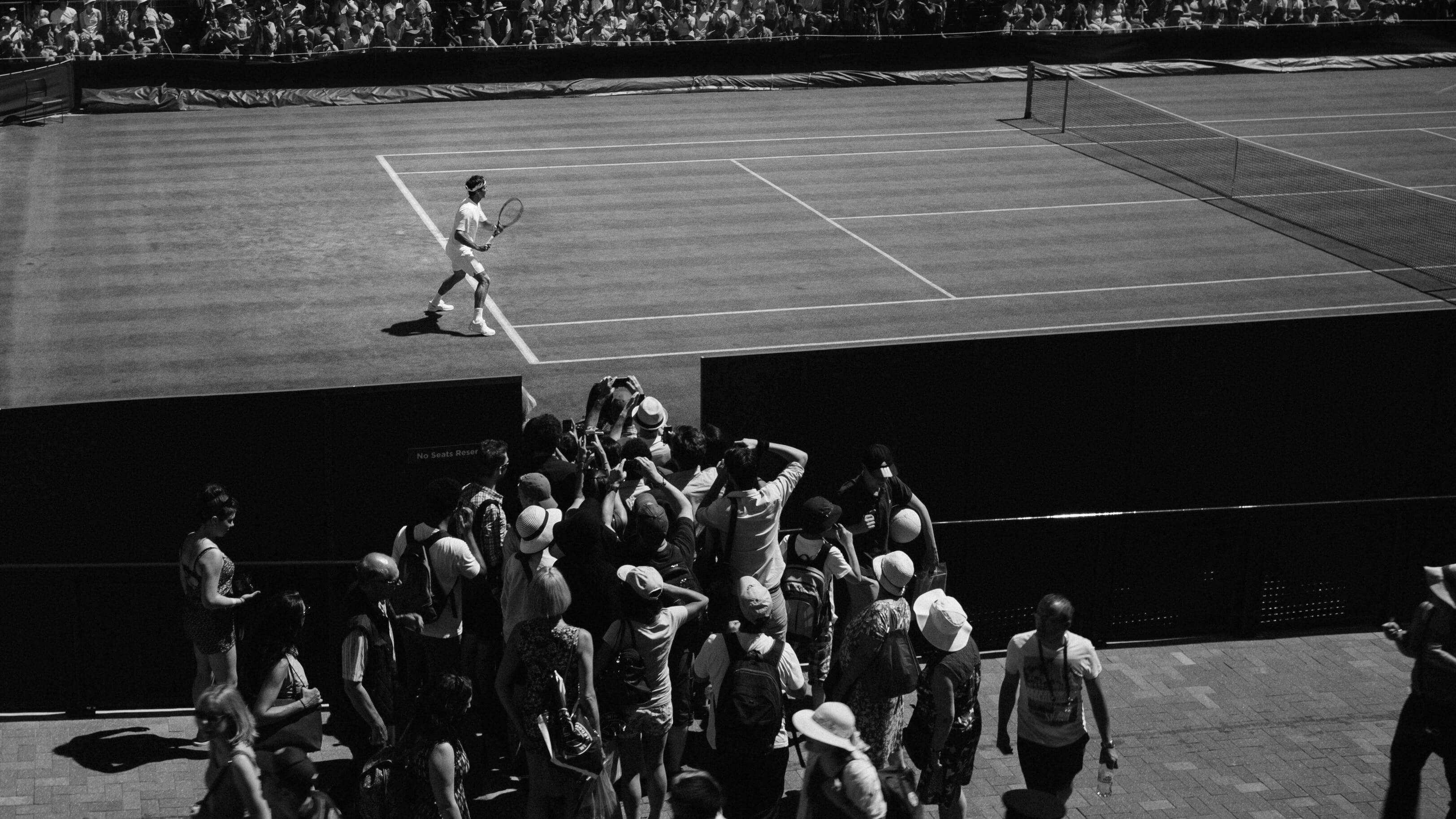 Wimbledon 桌布 壁紙 — 一張黑白高角度拍攝的網球選手在球場上行走，球迷擠滿邊線的照片。