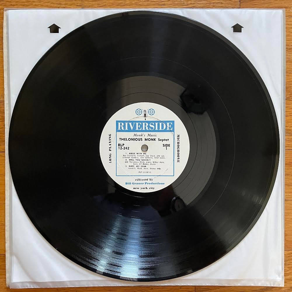 手機 桌布 壁紙 — 一張黑色黑膠唱片，白色標籤上寫著「Riverside Thelonious Monk Septet」，放在白色封套內，置於木質表面上。
