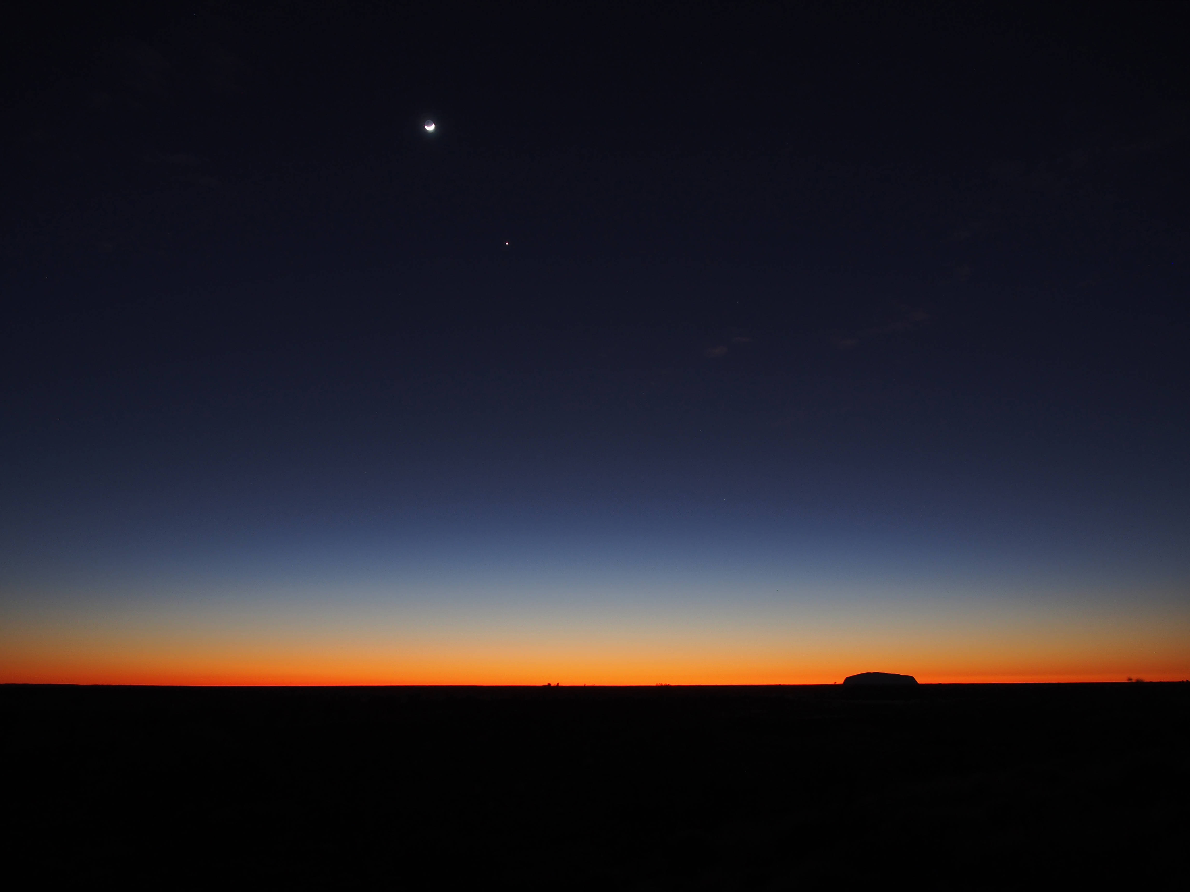 夜空 桌布 壁紙 — 一彎新月和一顆星星在黑暗的地平線上方閃耀，地平線在平坦的沙漠景觀上散發著橙色的暮光。