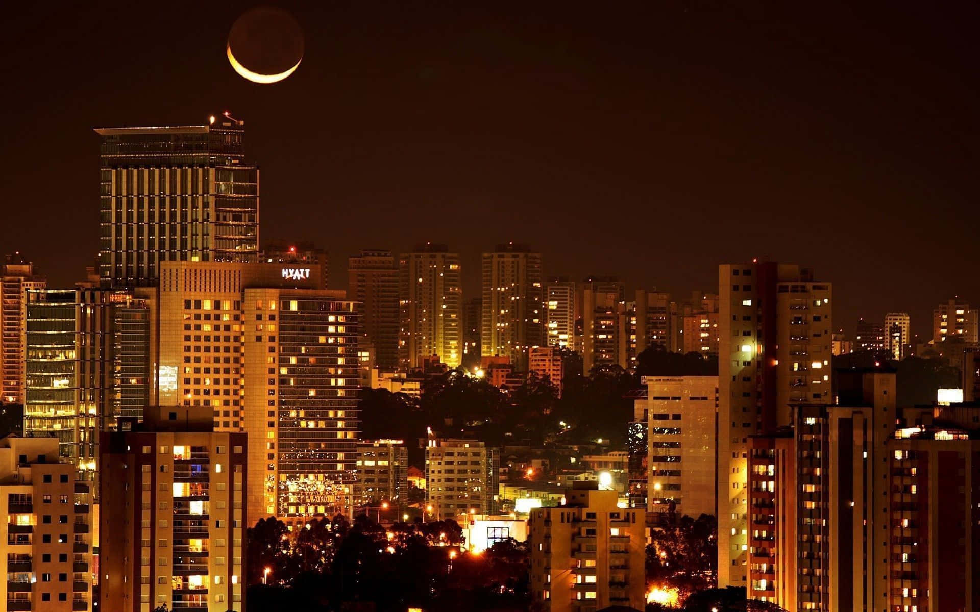 Mumbai 桌布 壁紙 — 一彎新月在夜晚照耀著廣闊的城市景觀，高樓大廈燈火通明，溫暖的金色燈光閃爍。